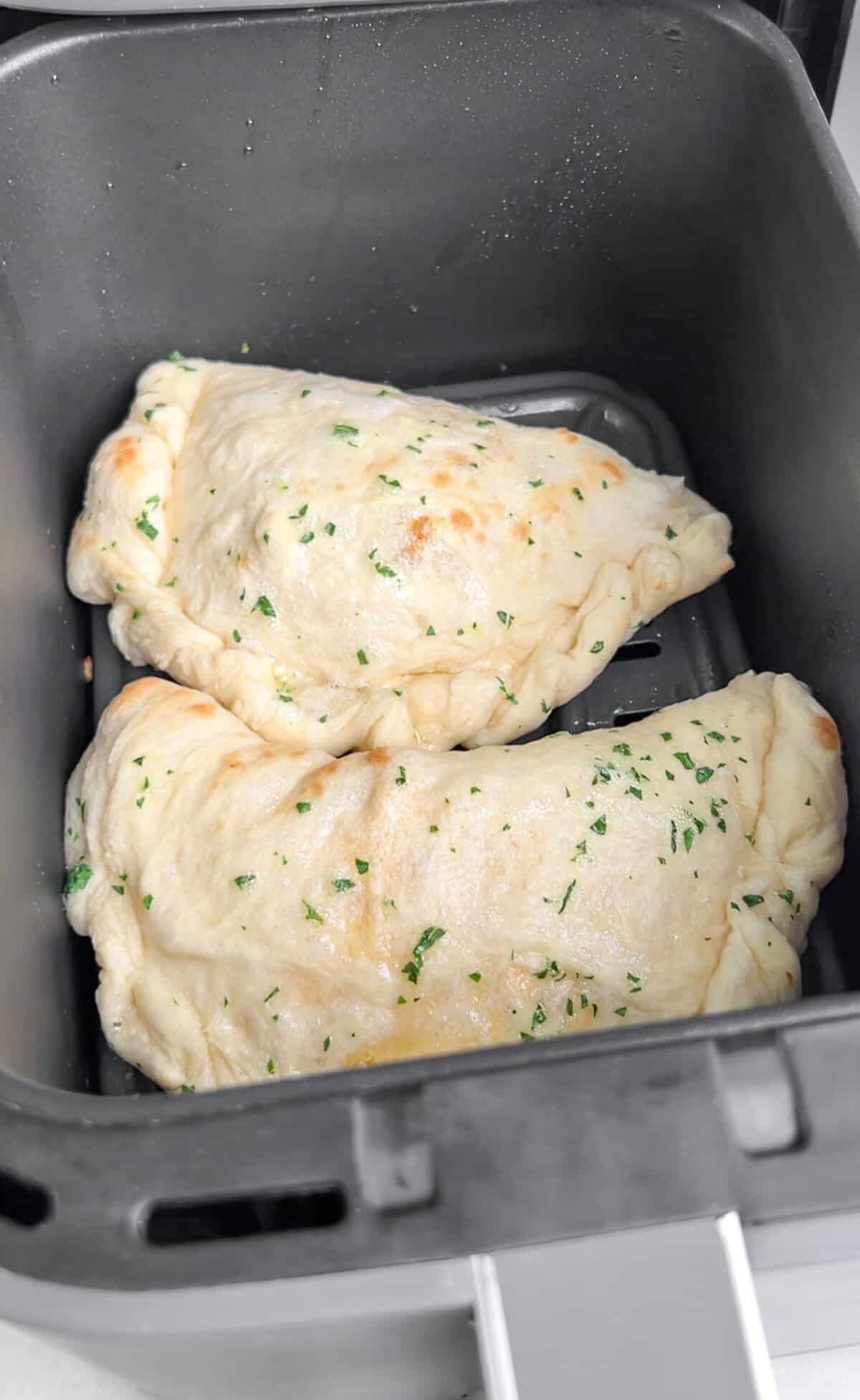 Pockets of dough are stuffed with your favorite pizza toppings, sauce, and cheese in these super easy Air Fryer Calzones. Two unbaked air fryer calzones in an air fryer