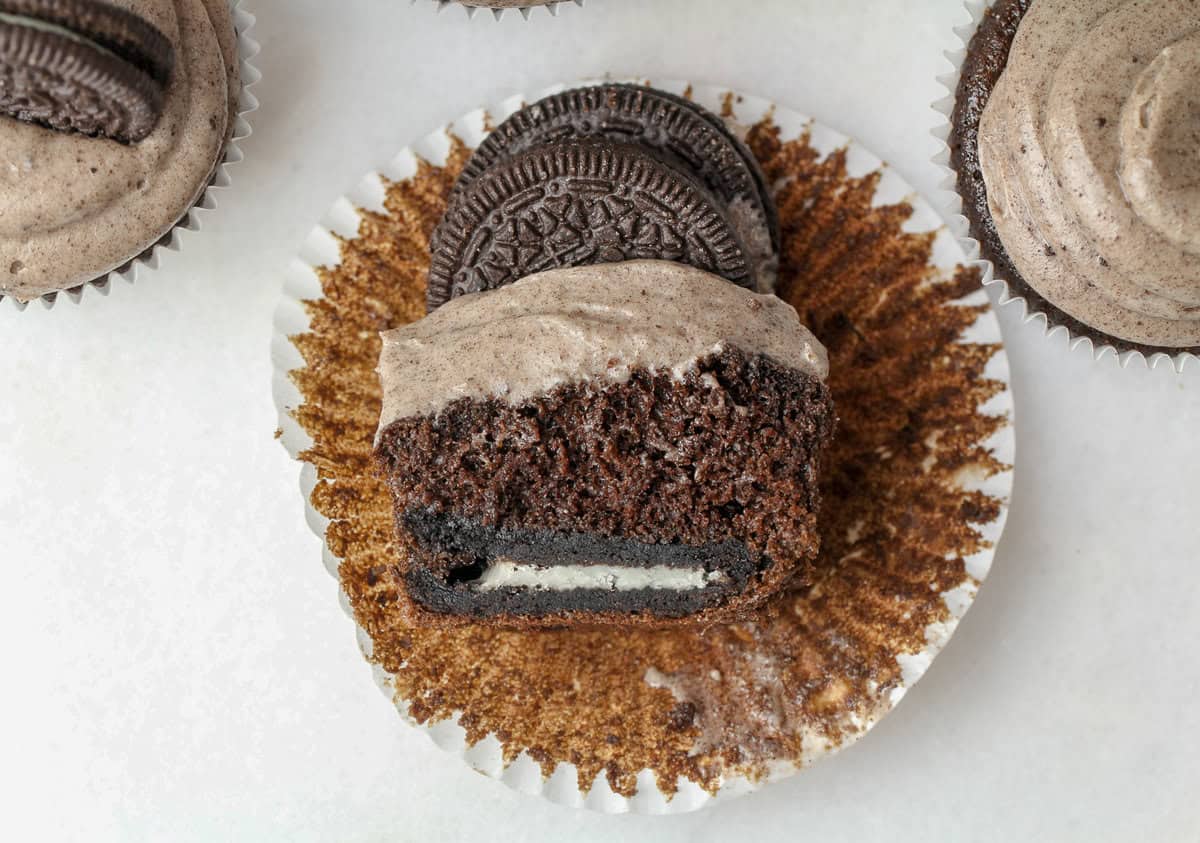 These super moist Oreo cupcakes have a hidden Oreo cookie inside, then topped with a cream cheese Oreo marshmallow frosting! Overhead view of half an Oreo cupcake on an unwrapped liner