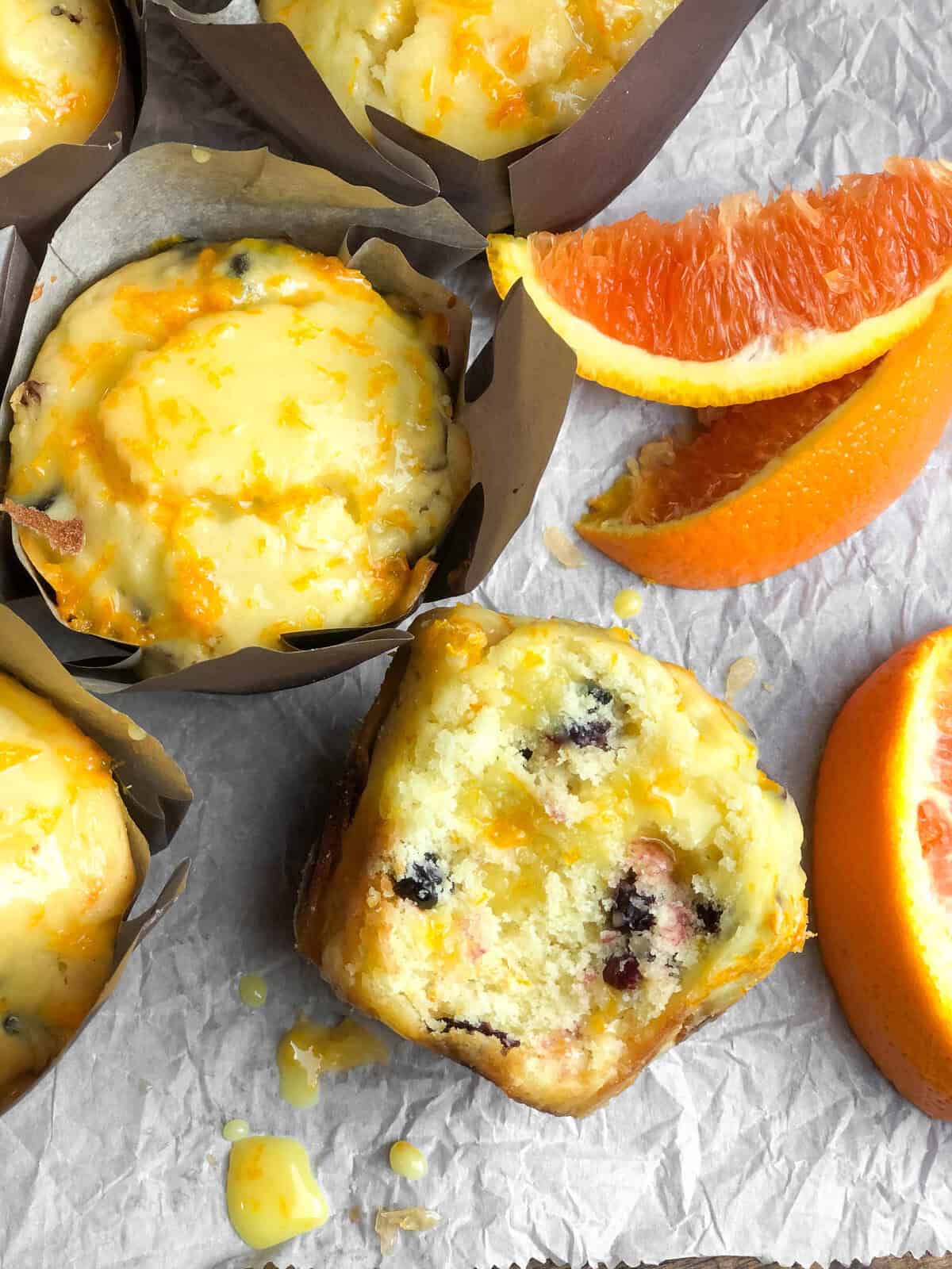 Tender, citrusy Orange Cranberry Muffins are buttery soft and topped with a tangy and vibrant orange glaze. No mixer needed! A table full of orange cranberry muffins next to orange slices