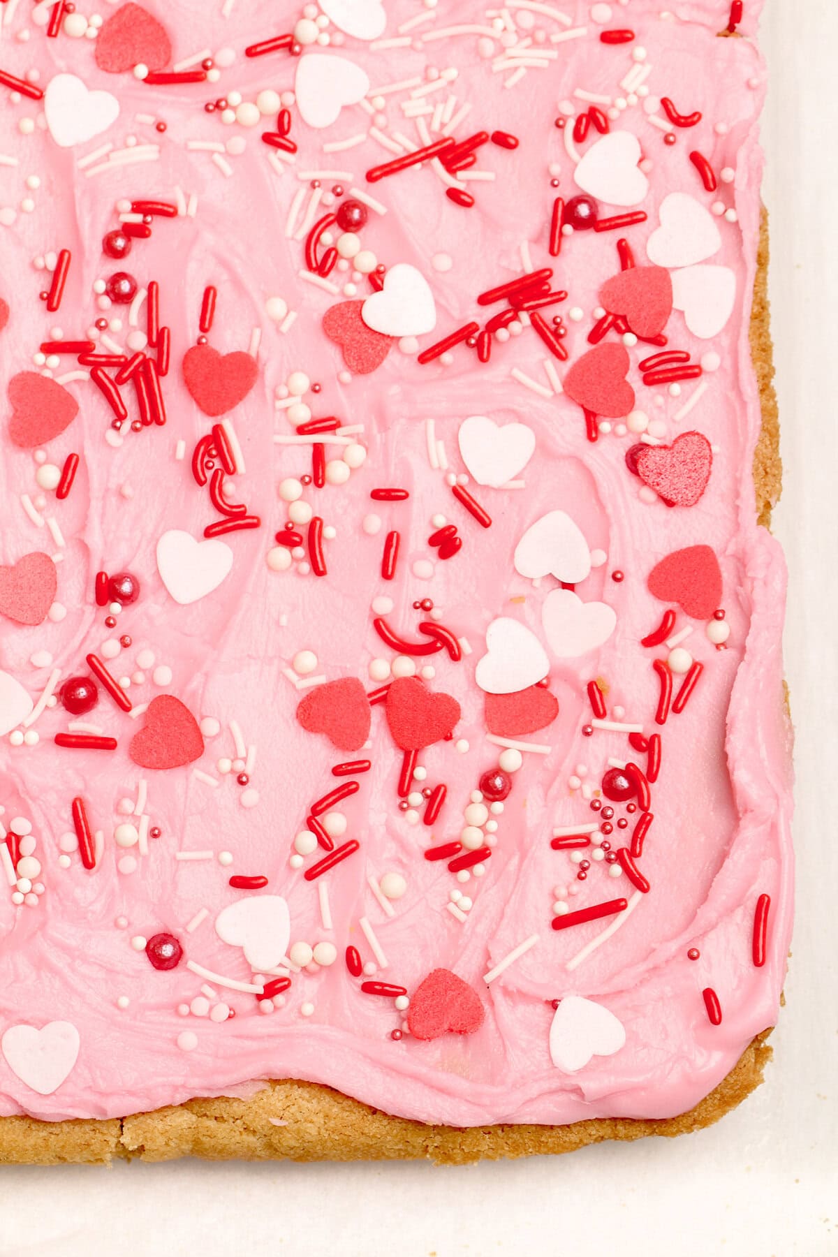 A thick, chewy cookie base is topped with a layer of sweet frosting and festive sprinkles in these frosted sugar cookie bars. Overhead view of the corner of a batch of frosted sugar cookie bars before being sliced.