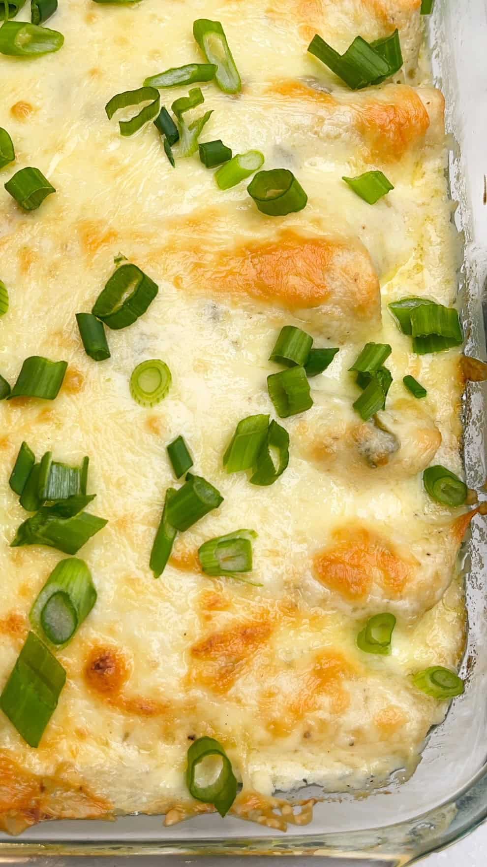 Seasoned chicken and shredded cheese are wrapped in tortillas and topped with a rich, tangy sauce in these White Chicken Enchiladas. A corner of a baking dish of white chicken enchiladas