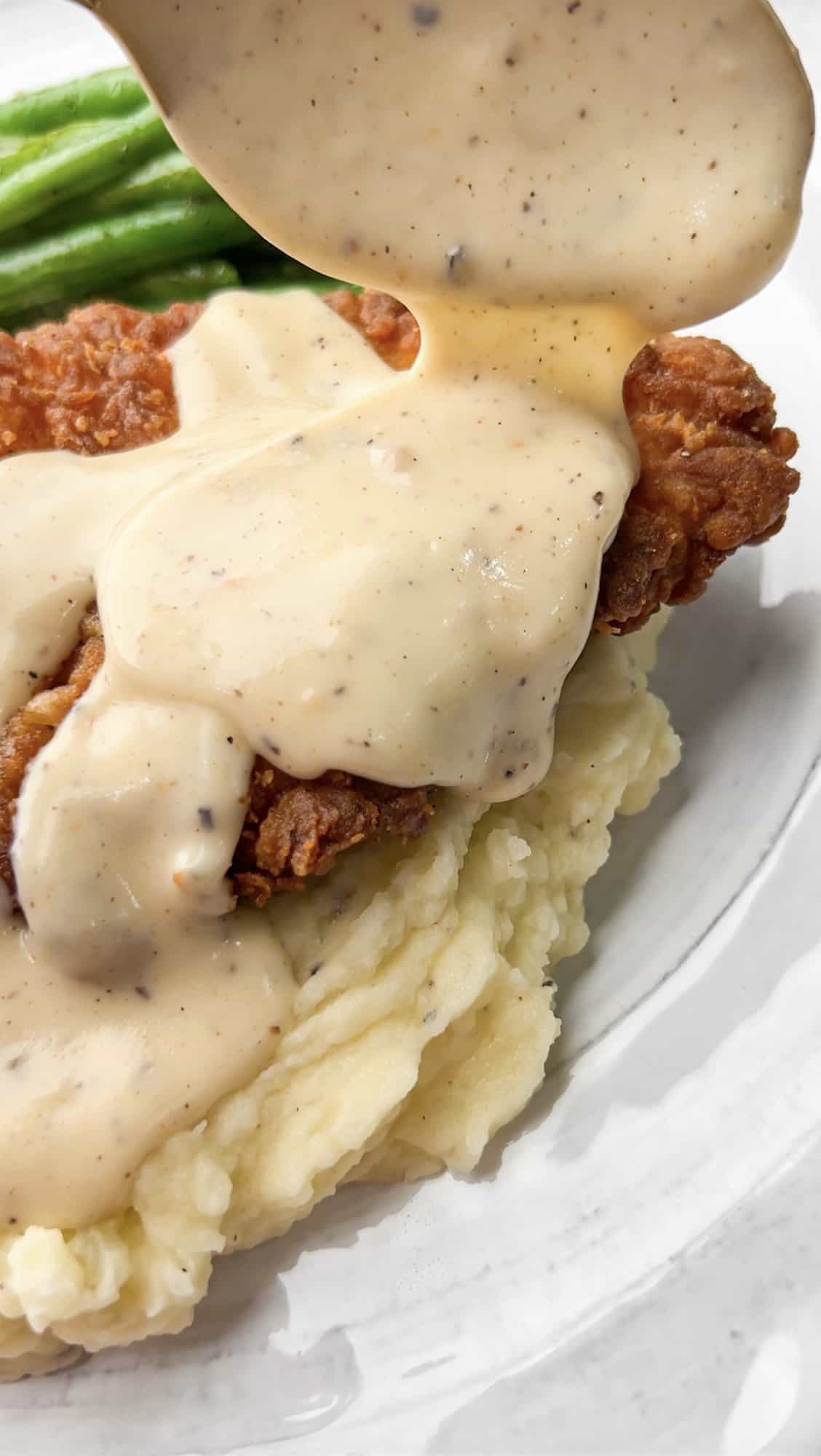 This Southern-style Chicken Fried Chicken is extra crispy and smothered in a flavorful white pepper gravy. Spooning gravy over chicken fried chicken