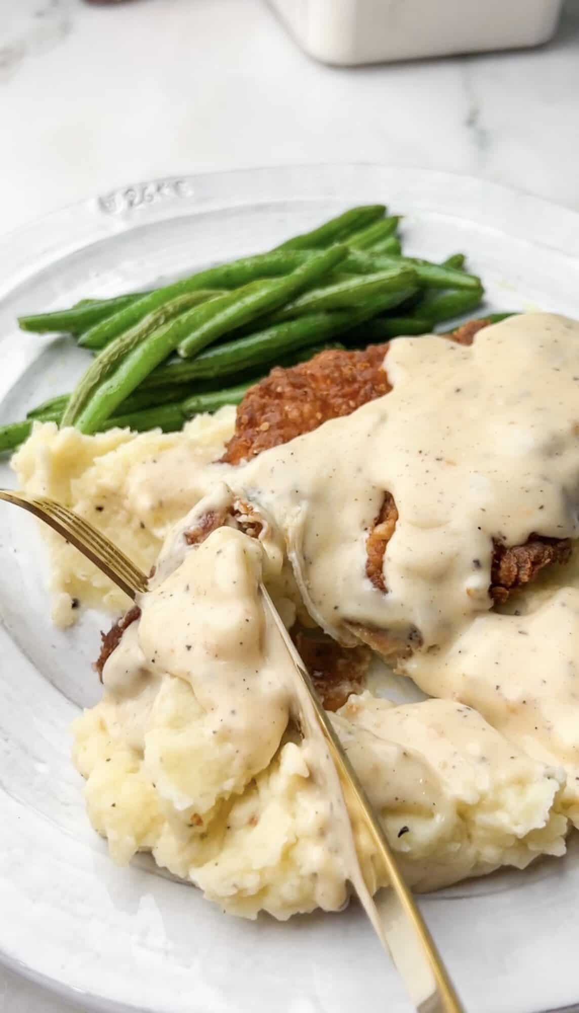 This Southern-style Chicken Fried Chicken is extra crispy and smothered in a flavorful white pepper gravy. A plate of chicken fried chicken with mashed potatoes and green beans