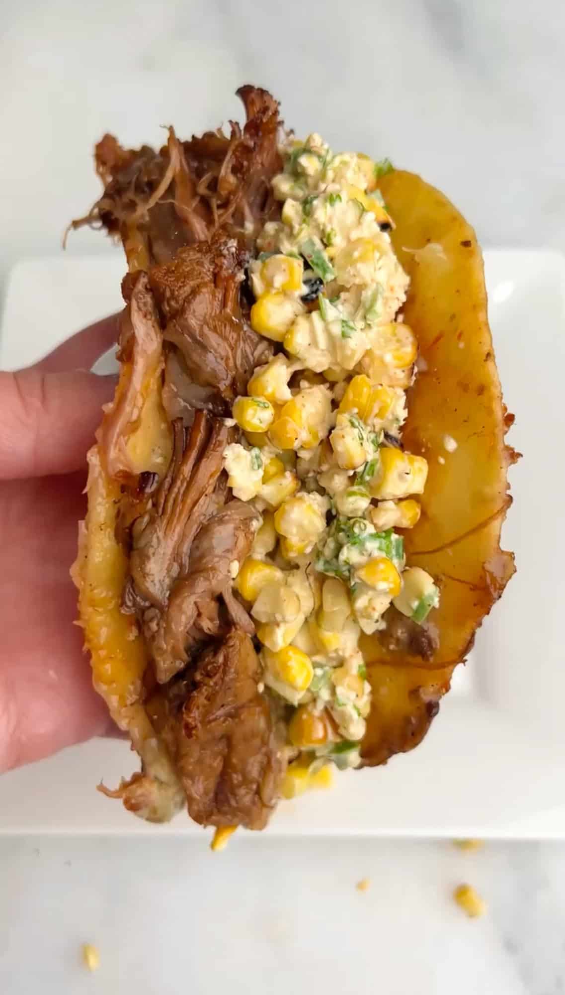 These Braised Brisket Tacos are pan-fried with melty cheese then topped with tangy street corn salad and creamy jalapeno lime ranch. A hand holding a brisket taco with street corn