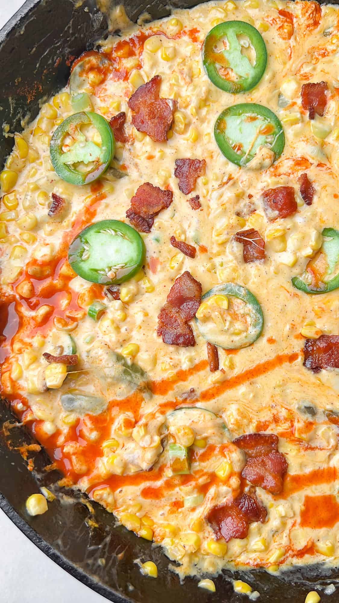 This Hot Corn Dip is bubbling hot and loaded with kicks of heat and pops of sweet corn, all intertwined with gooey melty cheese. Overhead view of a skillet of hot corn dipped with sliced jalapenos on top