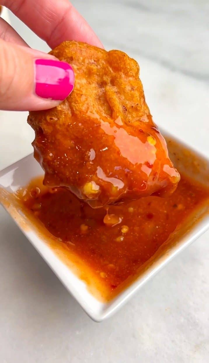 A spicy version of McDonald's Chicken Nugget recipe and Mighty Hot Sauce. These spicy chicken nuggets are super crispy, juicy and addictive. A hand dipping a spicy chicken nugget in mighty hot sauce