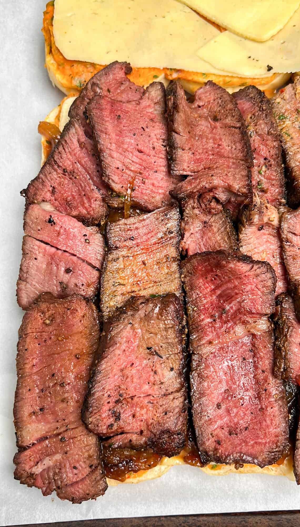These tender grilled steak sliders are smothered in lemony, herby cowboy butter and layers of melty havarti cheese. Perfect for game day! Sliced grilled steak on a cutting board, ready to be assembled into sliders.