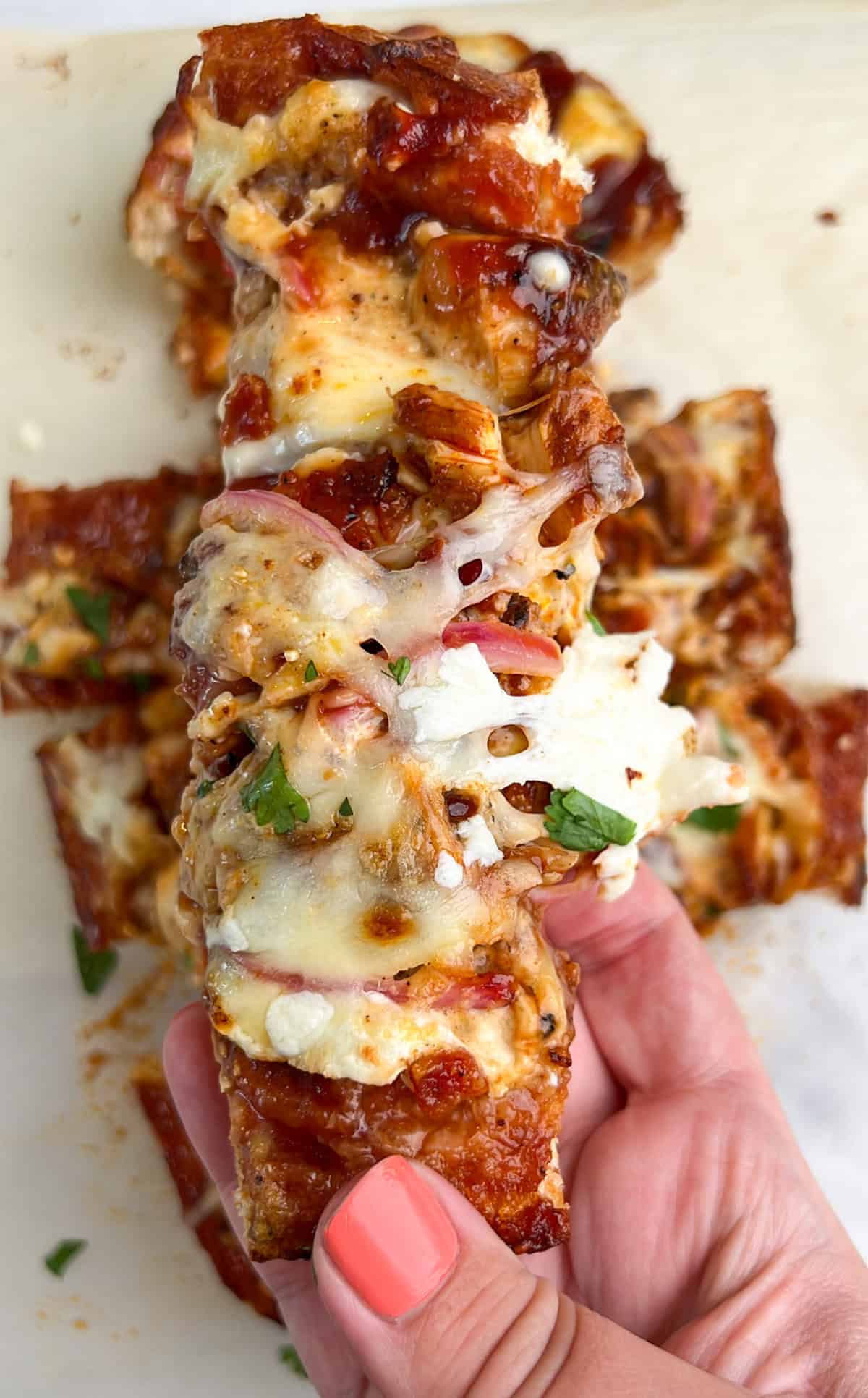 Crusty French bread is topped with sauce, cheese, and any toppings of choice, and then baked in this French Bread Pizza recipe. A hand holding a slice of BBQ chicken French bread pizza