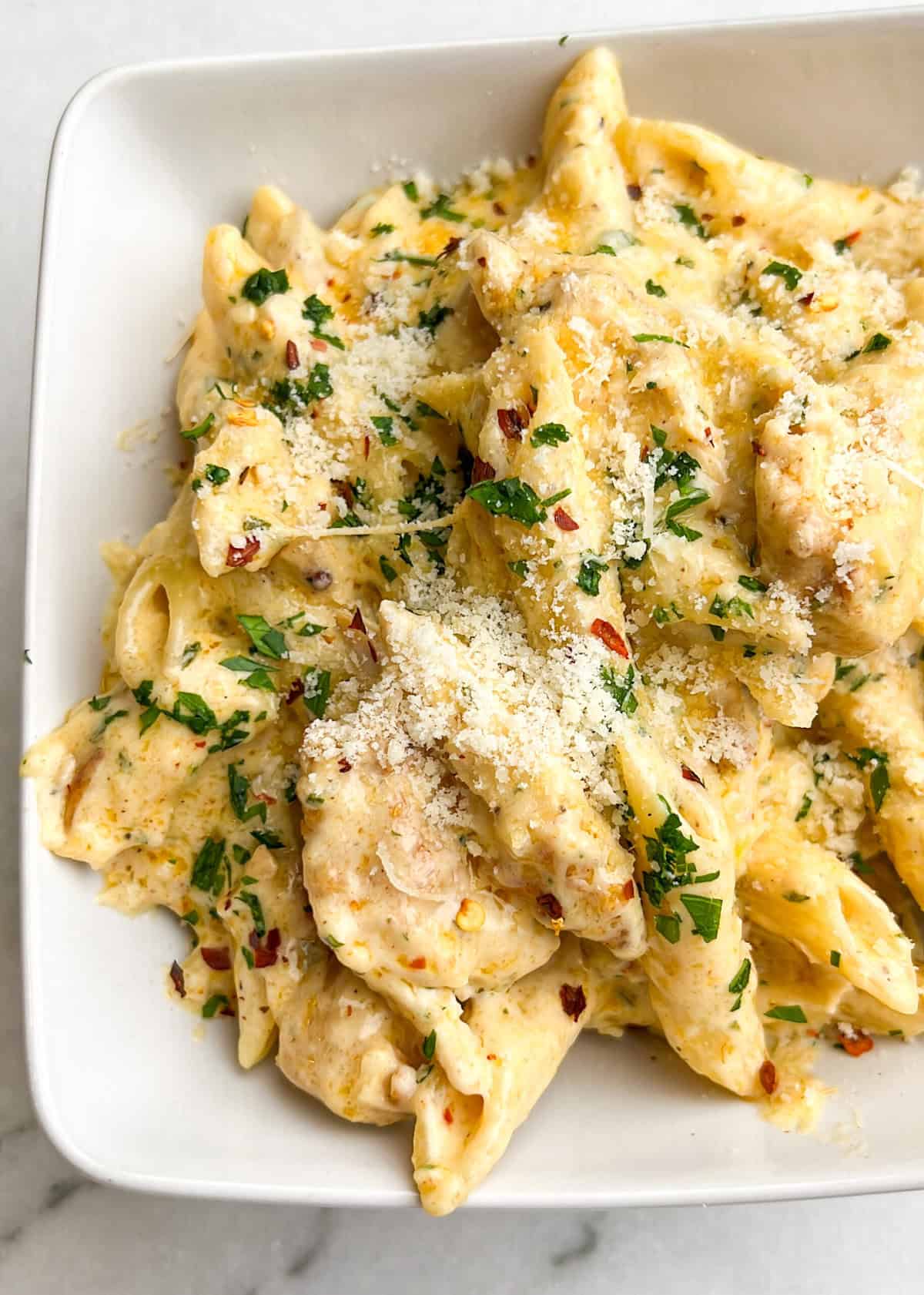 With juicy chicken and homemade garlic parm sauce over penne, Garlic Parmesan Chicken Pasta is an easy 30-minute dinner. Overhead view of a white bowl of Garlic Parmesan Chicken Pasta