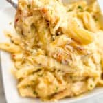 Close up of a forkful of garlic parmesan chicken pasta above a bowl of pasta