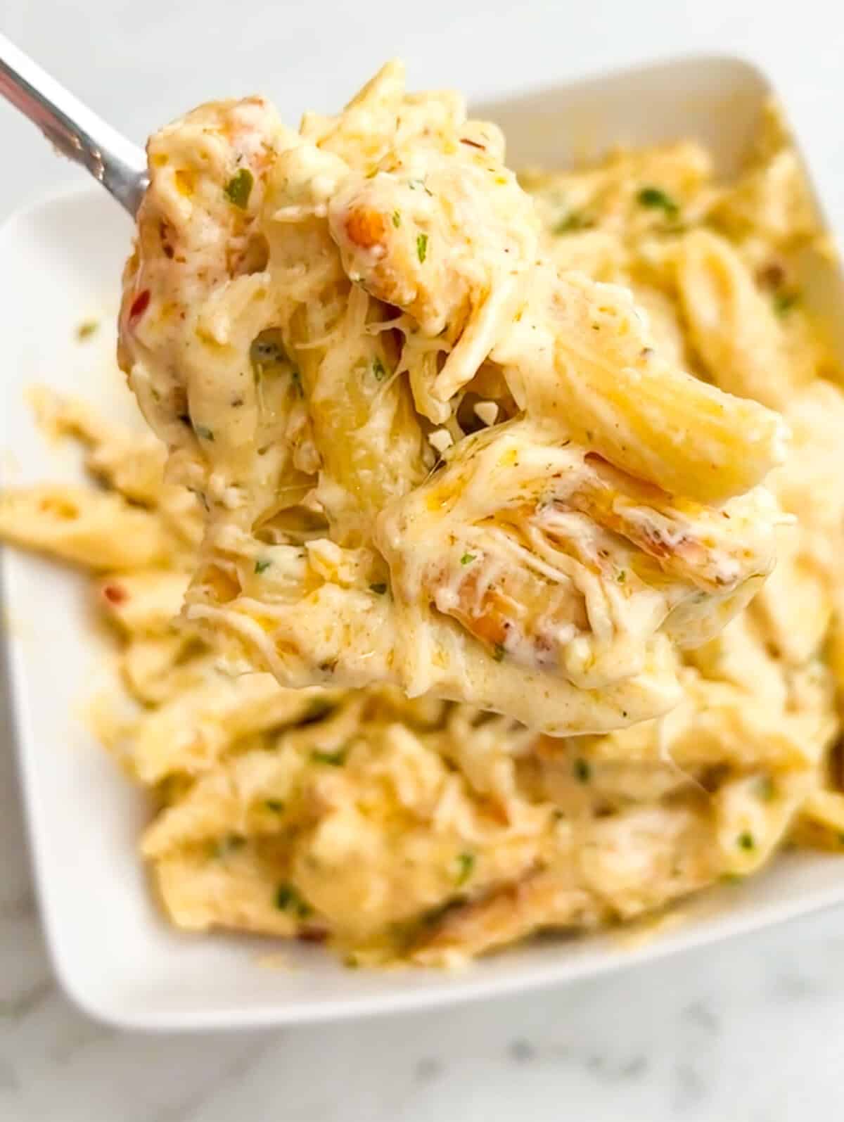 Close up of a forkful of garlic parmesan chicken pasta above a bowl of pasta