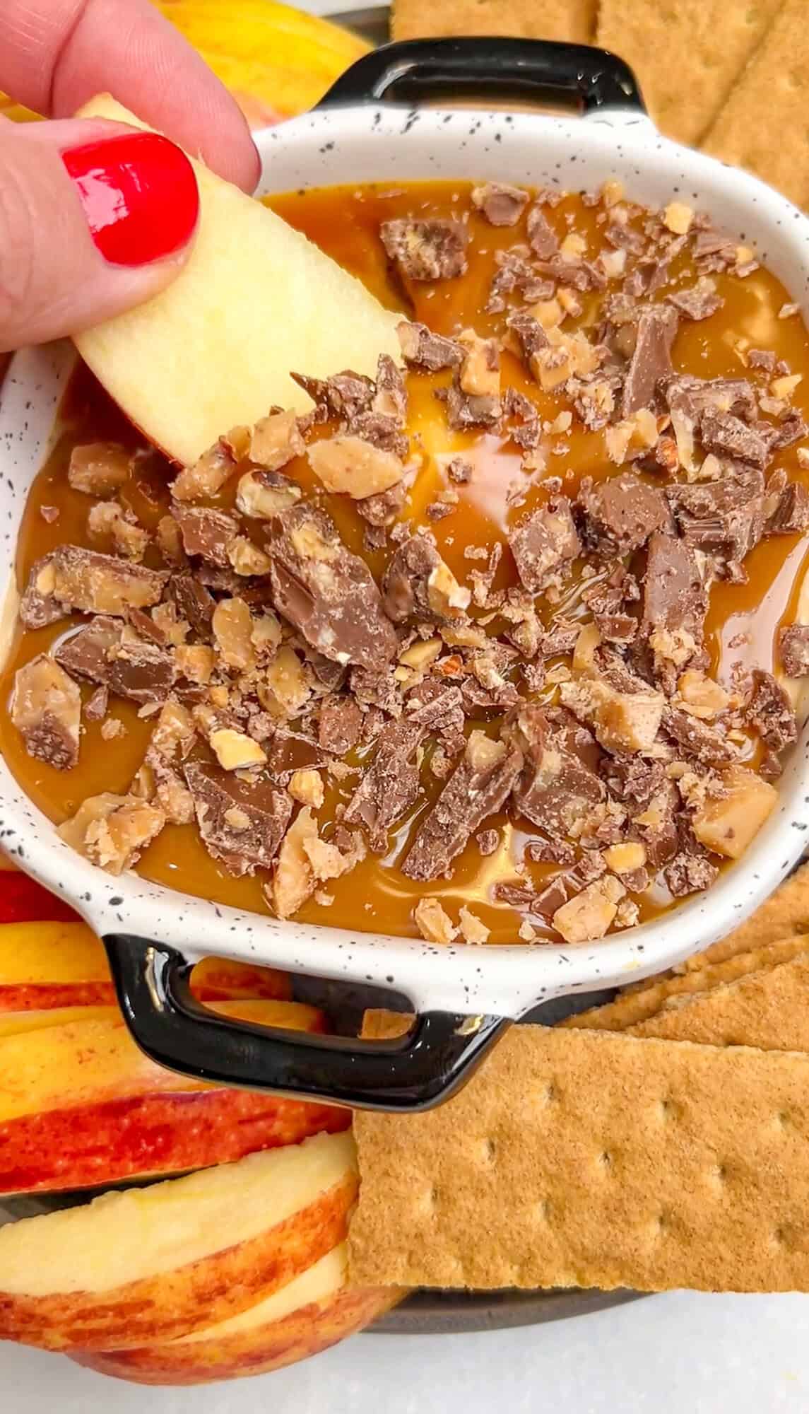 Caramel Apple Dip is a creamy, decadent dessert dip made with just 5 ingredients in 10 minutes. Perfect for fall! A hand dipping an apple slice into caramel apple dip