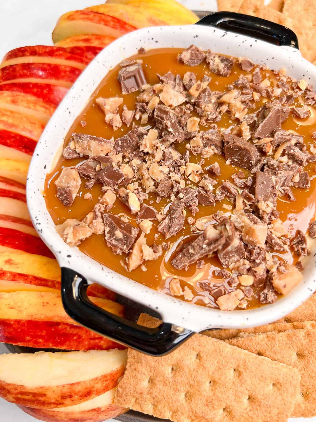 Caramel Apple Dip is a creamy, decadent dessert dip made with just 5 ingredients in 10 minutes. Perfect for fall! Close up of a bowl of caramel apple dip surrounded by apple slices and graham crackers