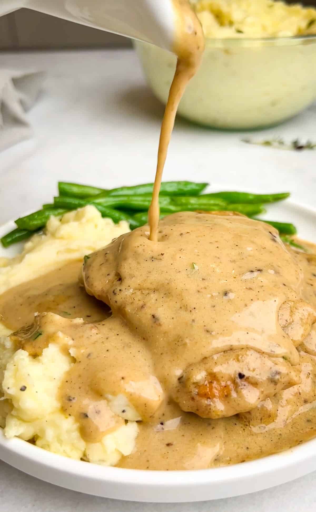 With a rich, mouth-watering sauce made from garlic, heavy cream, and parmesan, this creamy garlic chicken is comfort food at its finest. Pouring sauce over creamy garlic chicken on a plate with mashed potatoes and green beans