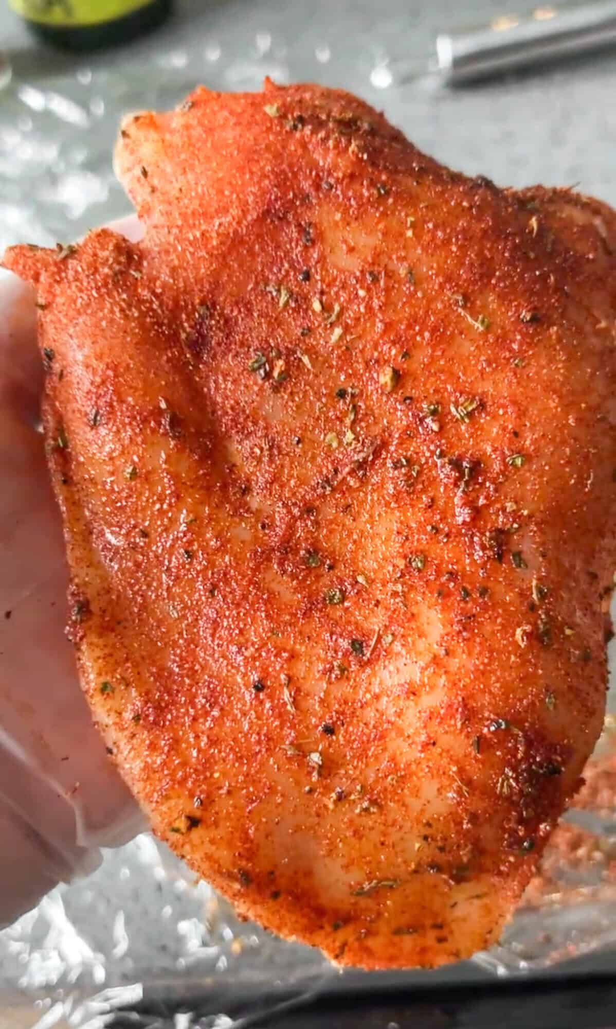 With juicy blackened chicken and a garlicky seasoned alfredo sauce, Blackened Chicken Alfredo is a quick and easy weeknight dinner. A hand holding an uncooked chicken breast with blackened seasoning