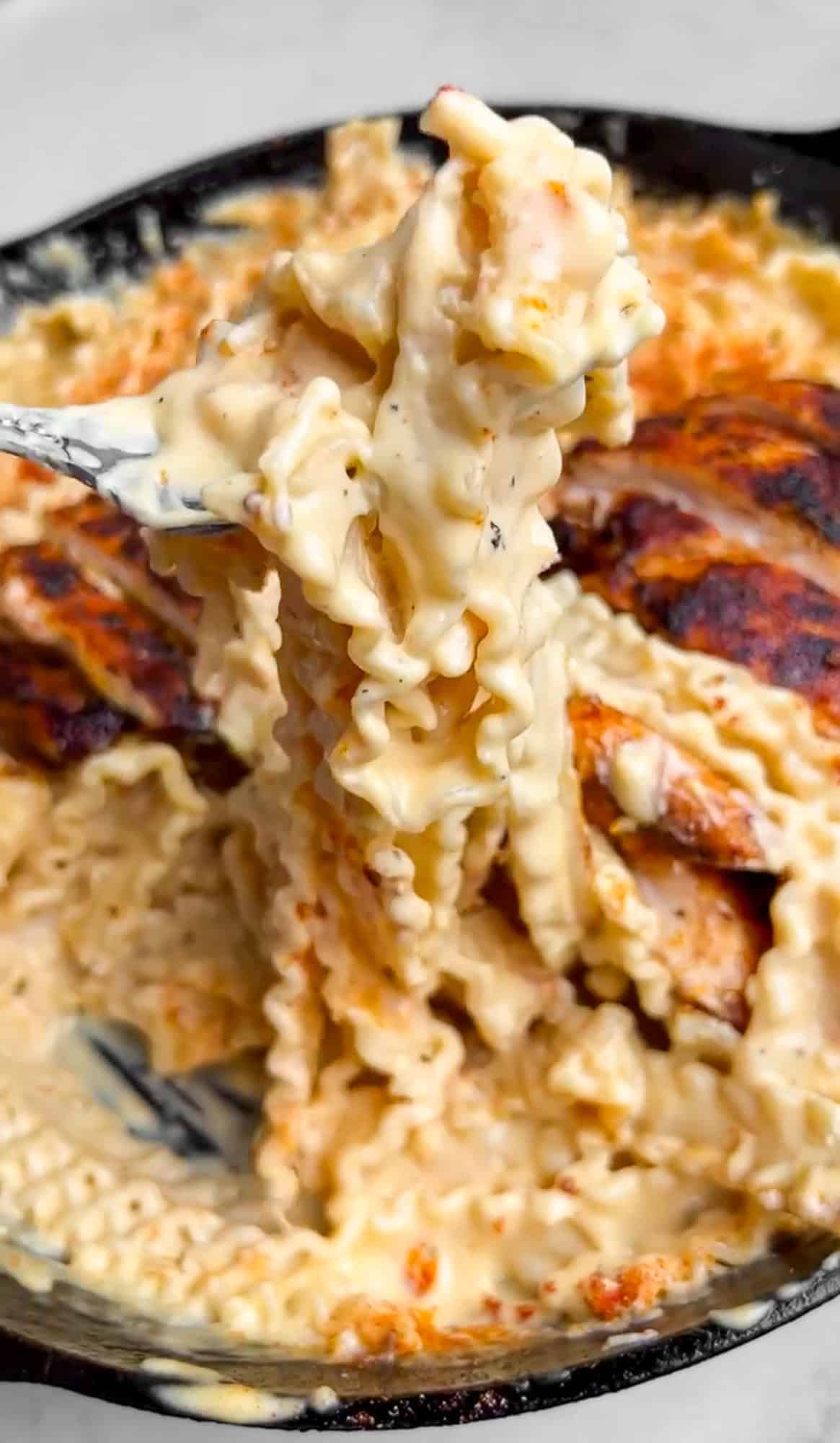 With juicy blackened chicken and a garlicky seasoned alfredo sauce, Blackened Chicken Alfredo is a quick and easy weeknight dinner. A fork holding pasta over a pan of blackened chicken alfredo