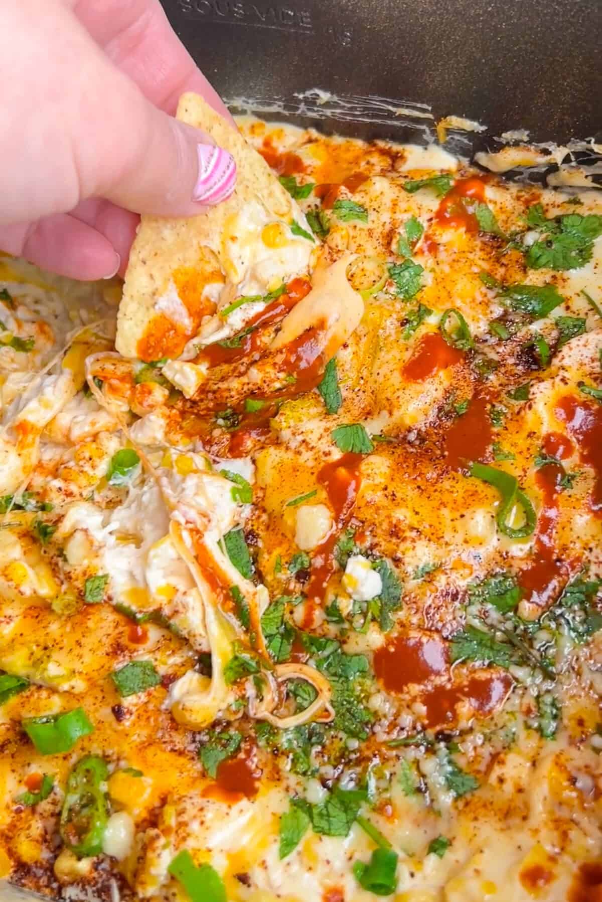 A hand dipping a tortilla into slow cooker Mexican street corn dip