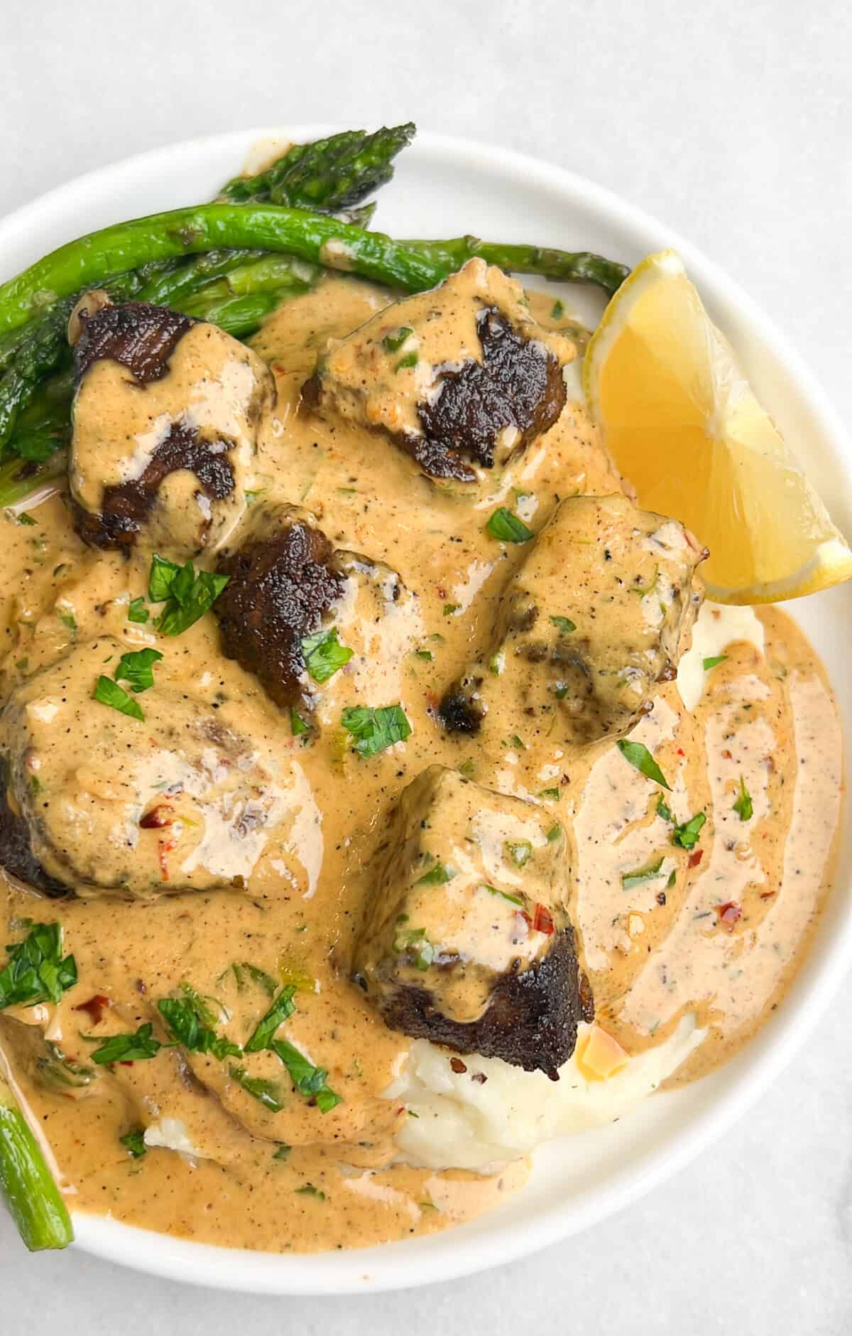 Overhead view of garlic butter steak bites served over mashed potatoes with a side of asparagus, smothered in creamy Parmesan sauce.
