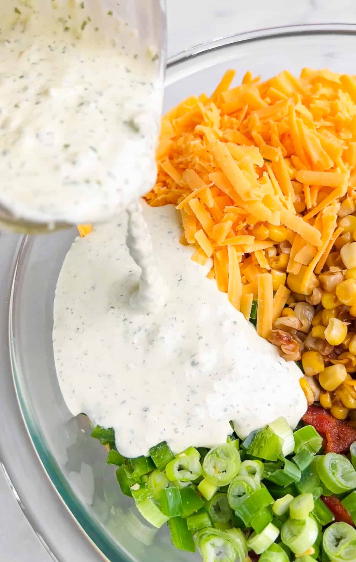With crispy bacon, kernels of corn, cheddar cheese, and jalapeños tossed in creamy jalapeño ranch, this crack corn salad is quick & easy. Adding jalapeno ranch to a bowl with green onions, cheese, corn, and bacon