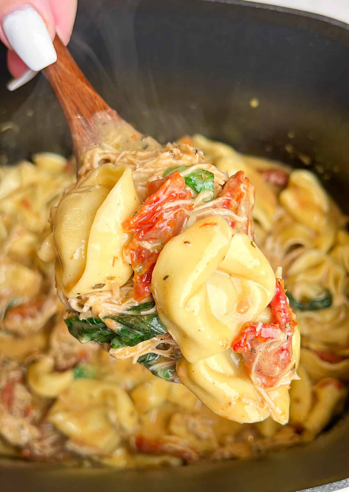 Marry me chicken tortellini is an easy slow cooker recipe, with tender chicken, tortellini, and basil in rich sun-dried tomato cream sauce. A spoonful of marry me chicken tortellini lifted from the slow cooker.