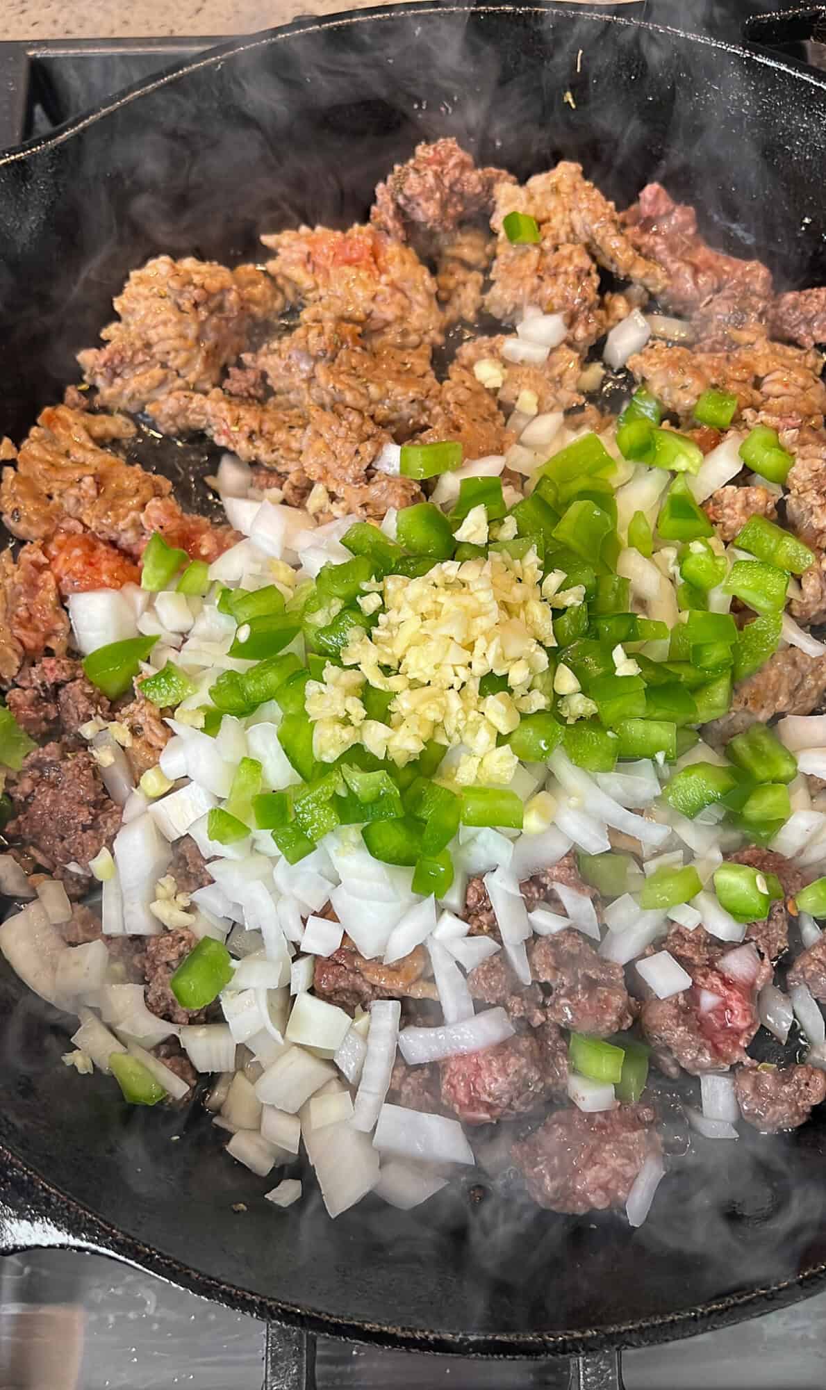 This baked Million Dollar Spaghetti recipe layers homemade alfredo sauce with marinara meat sauce, topped with a blanket of golden cheese. Ground beef, diced onions, and bell peppers combined in a pan.