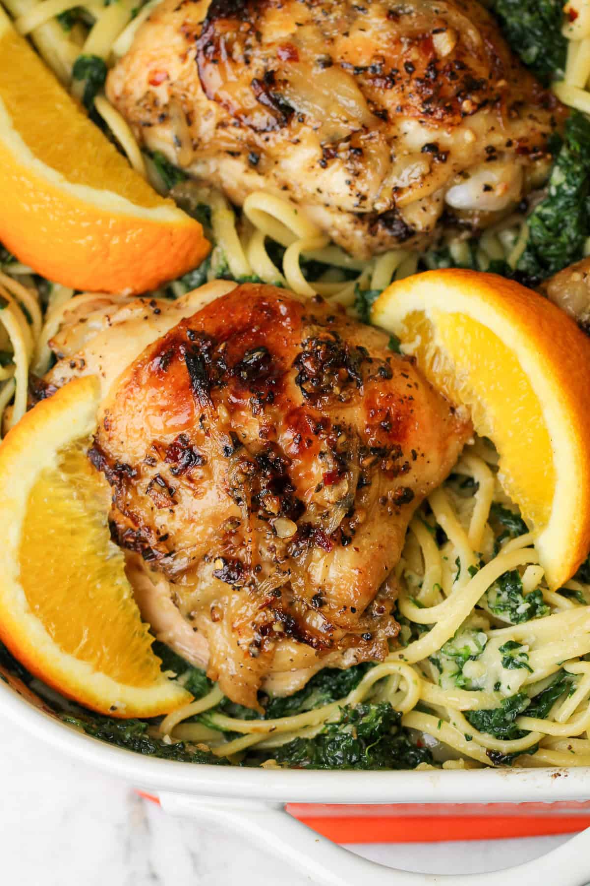 baked chicken with orange wedges over linguini