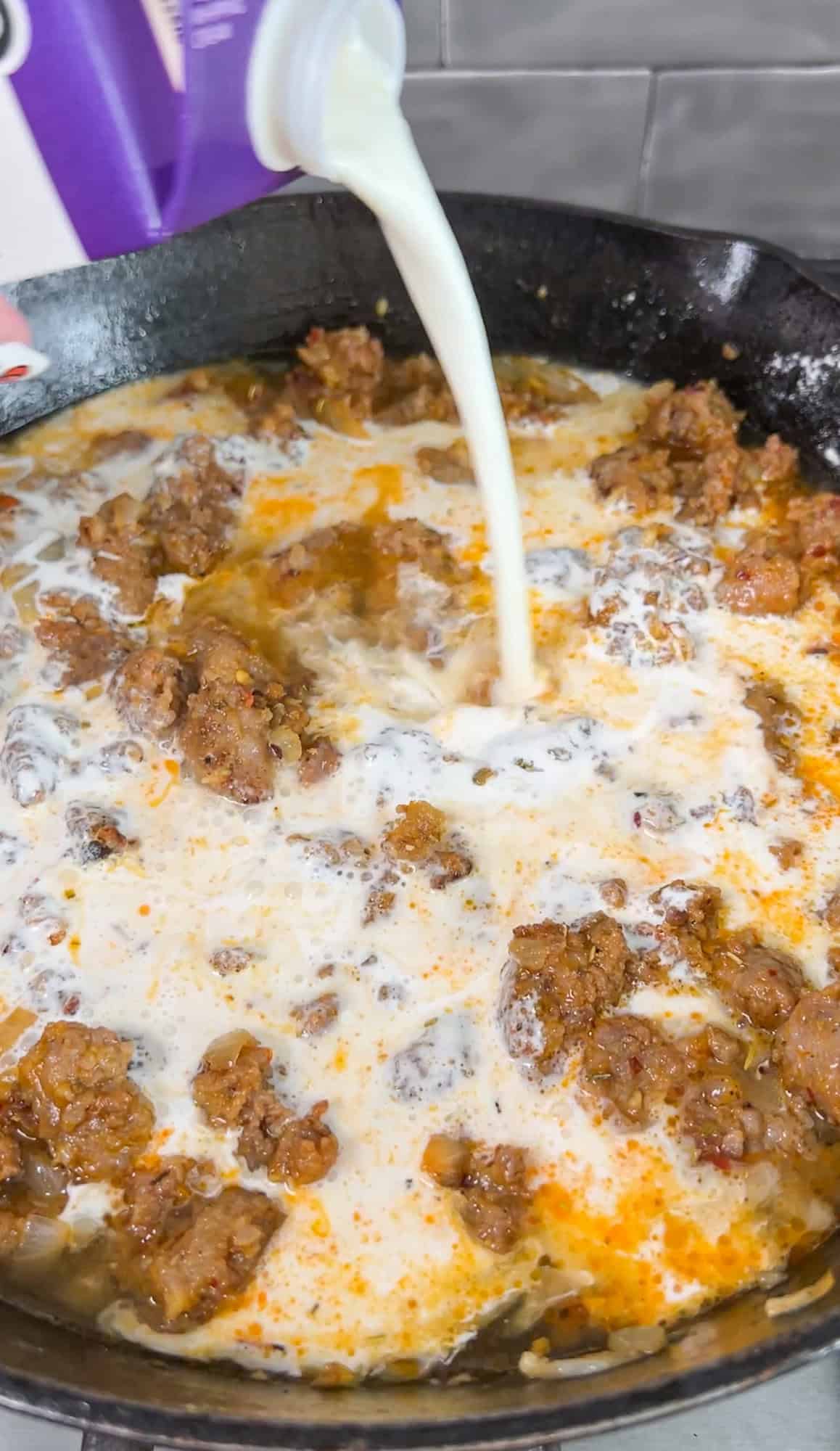 cream pouring into a pan of sausage