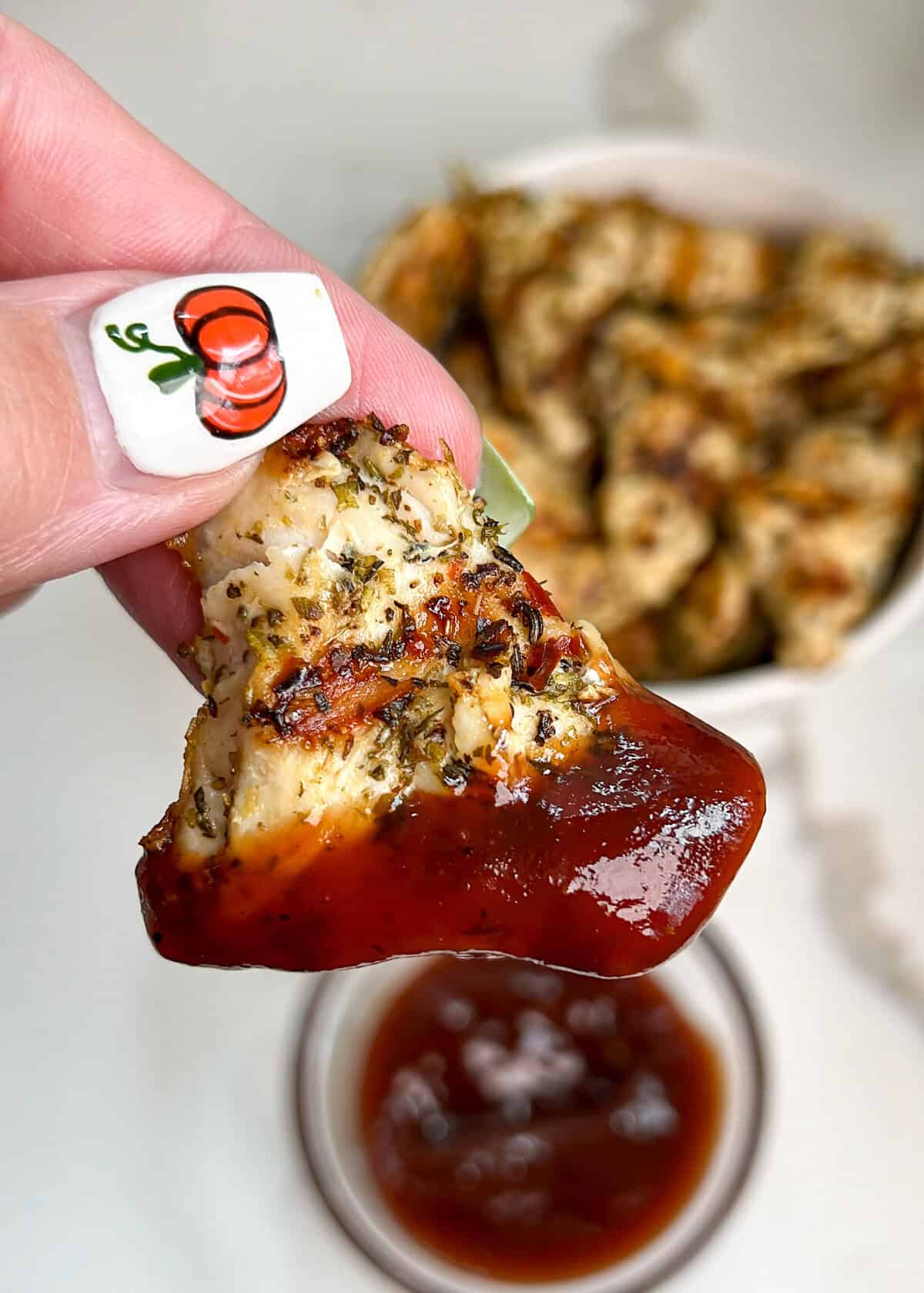 These smoky, tender and juicy chicken nuggets are easily grilled up on the stove in this copycat Chick fil A Grilled Nuggets recipe. A hand holding a grilled chicken nugget dipped in BBQ sauce
