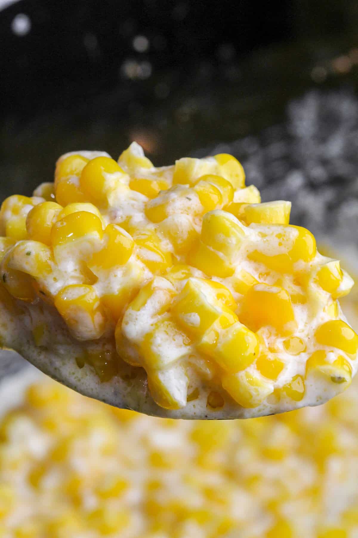 This crock pot creamed corn is sweet and savory with just the right amount of tang. It's the ultimate set-it-and-forget-it holiday recipe. A spoon scooping creamed corn out of a slow cooker.