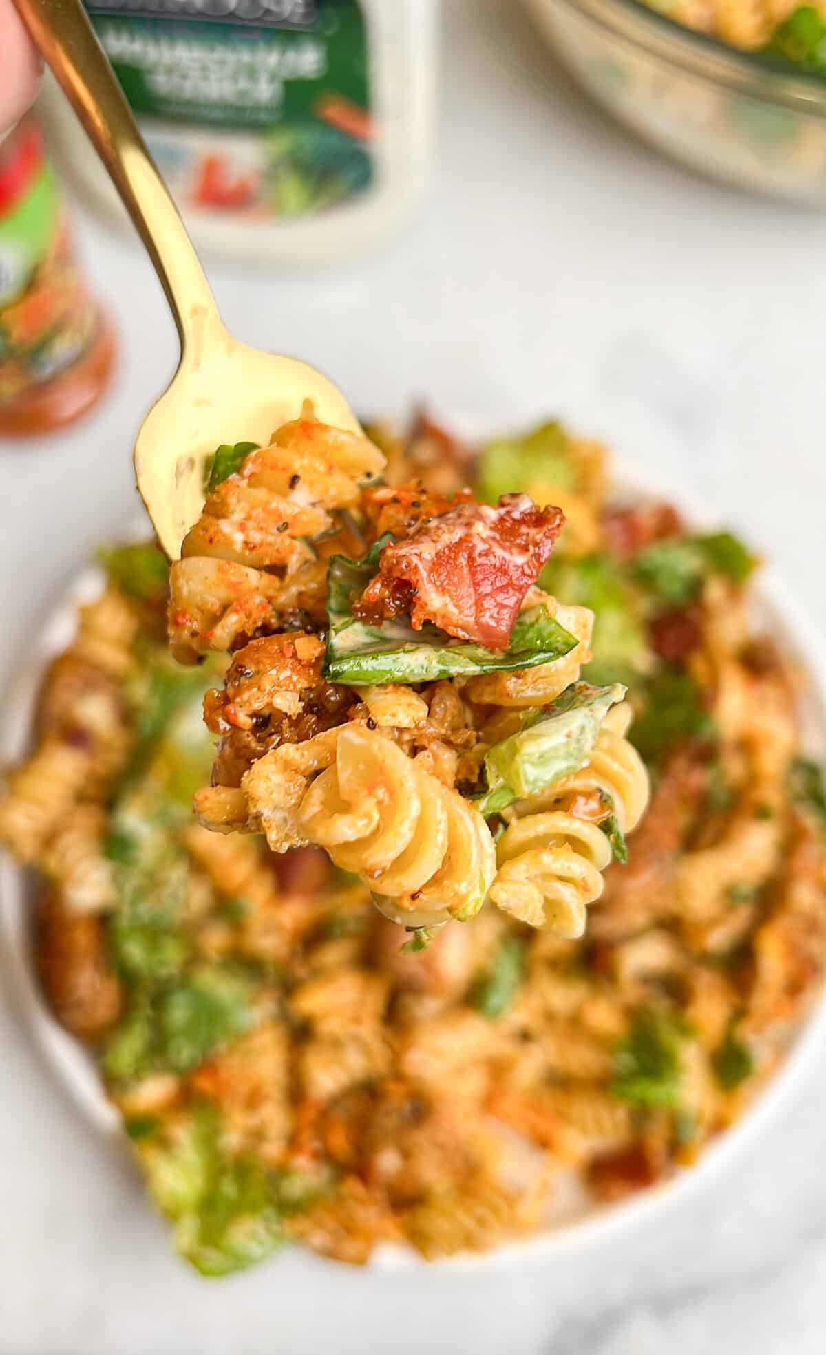 Diced chicken, crispy bacon, crunchy romaine lettuce, and croutons are tossed with ranch dressing in this Chicken Bacon Ranch Pasta Salad. A forkful of chicken bacon ranch pasta salad above a bowl