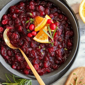 A serving bowl full of homemade cranberry sauce with a golden spoon.