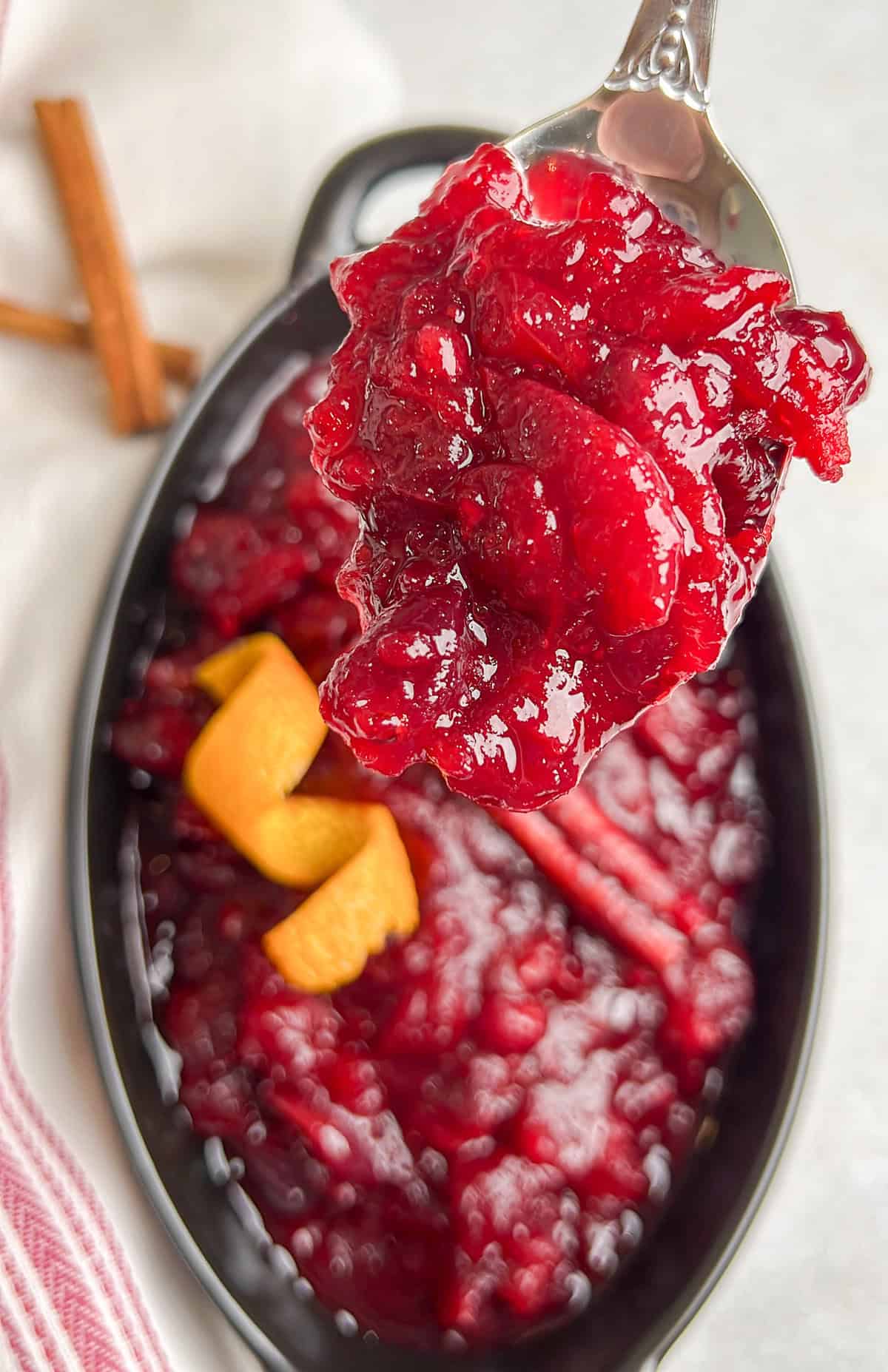 Skip the canned stuff this year. This 20-minute cranberry sauce is made from fresh cranberries, with a hint of orange and warming cinnamon. A serving spoon holding a scoop of homemade cranberry sauce up to the camera.