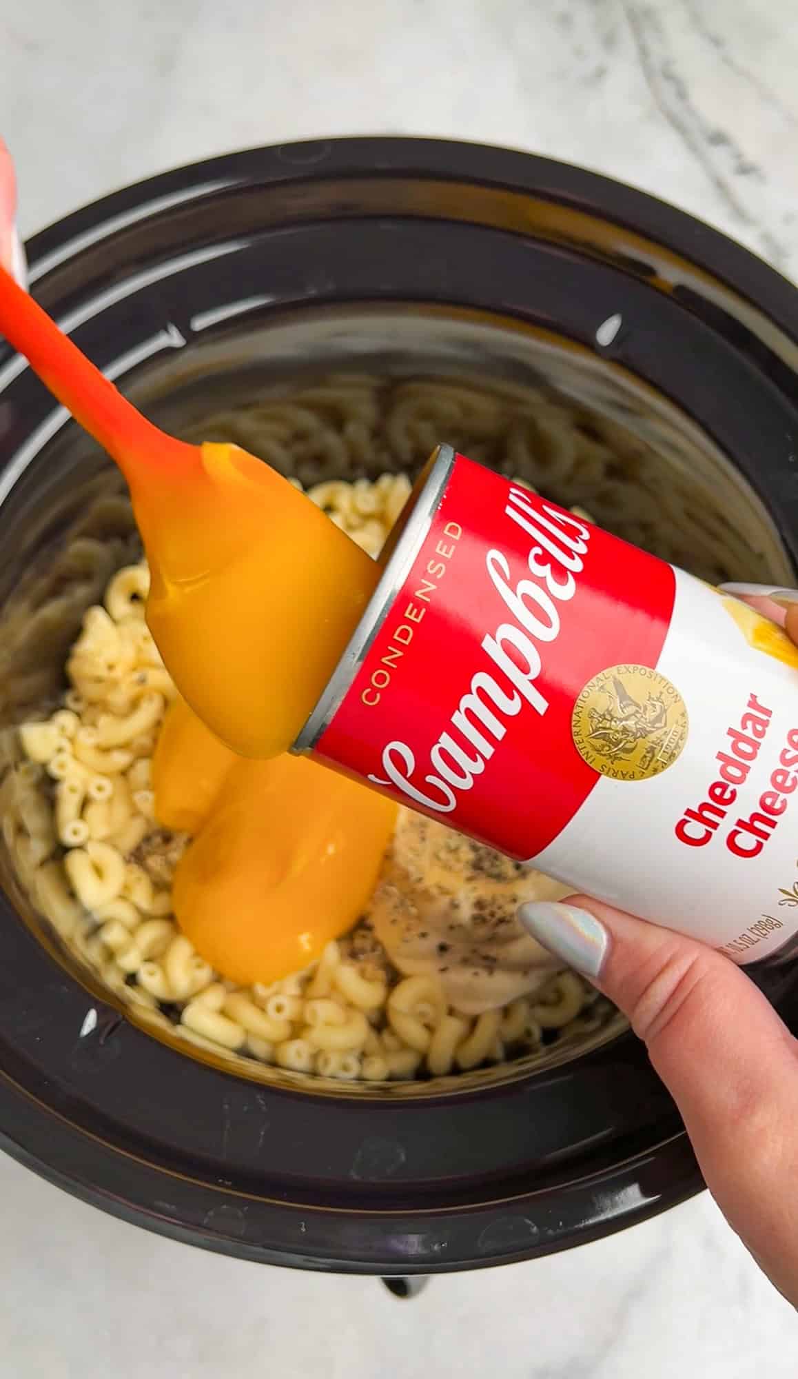 condensed soup being poured over macaroni in the slow cooker