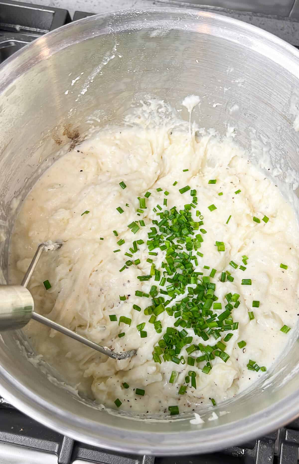 adding chives to the mashed potatoes in a pot