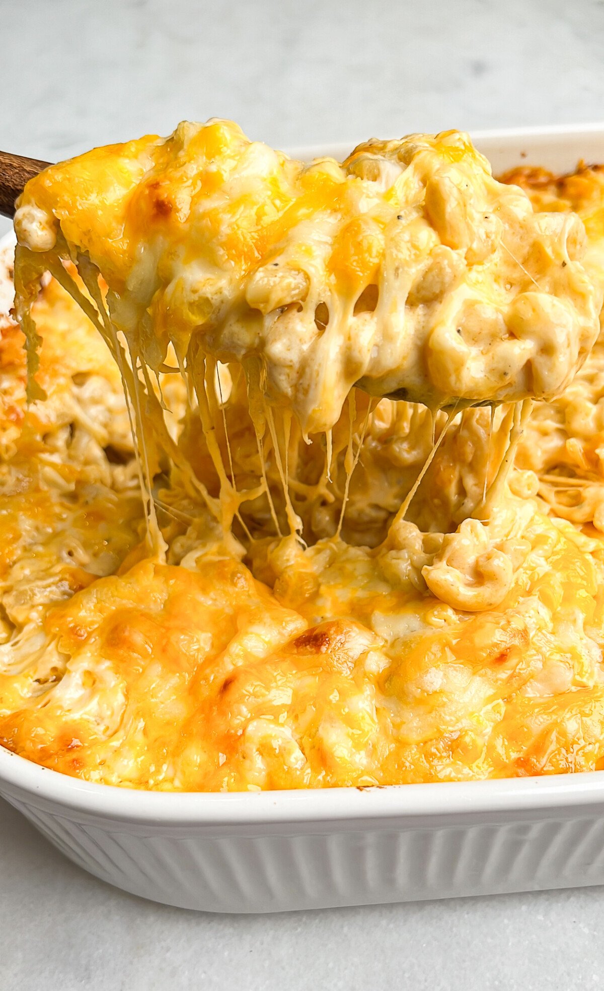 gooey macaroni and cheese being lifted out of pan with a spoon