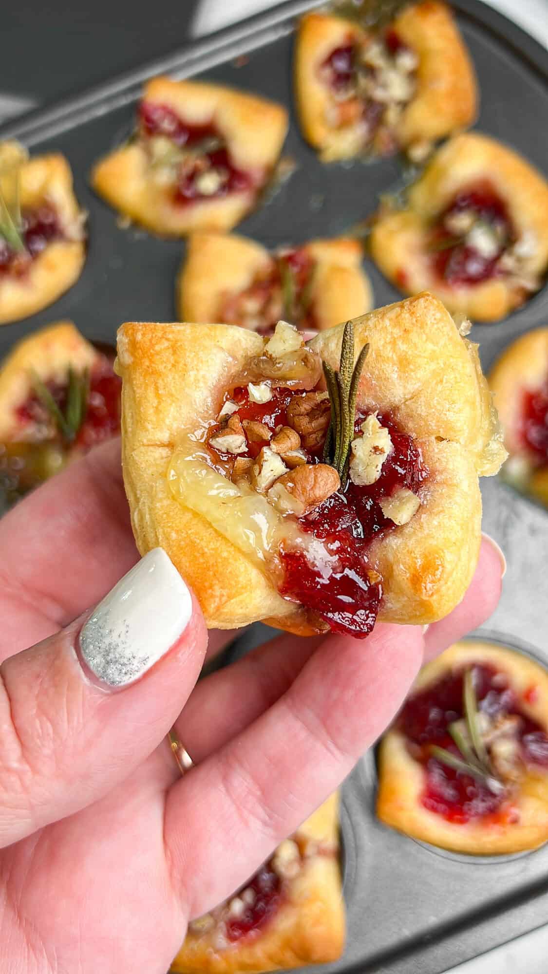 baked brie cranberry bites baked in puff pastry, being held in a hand