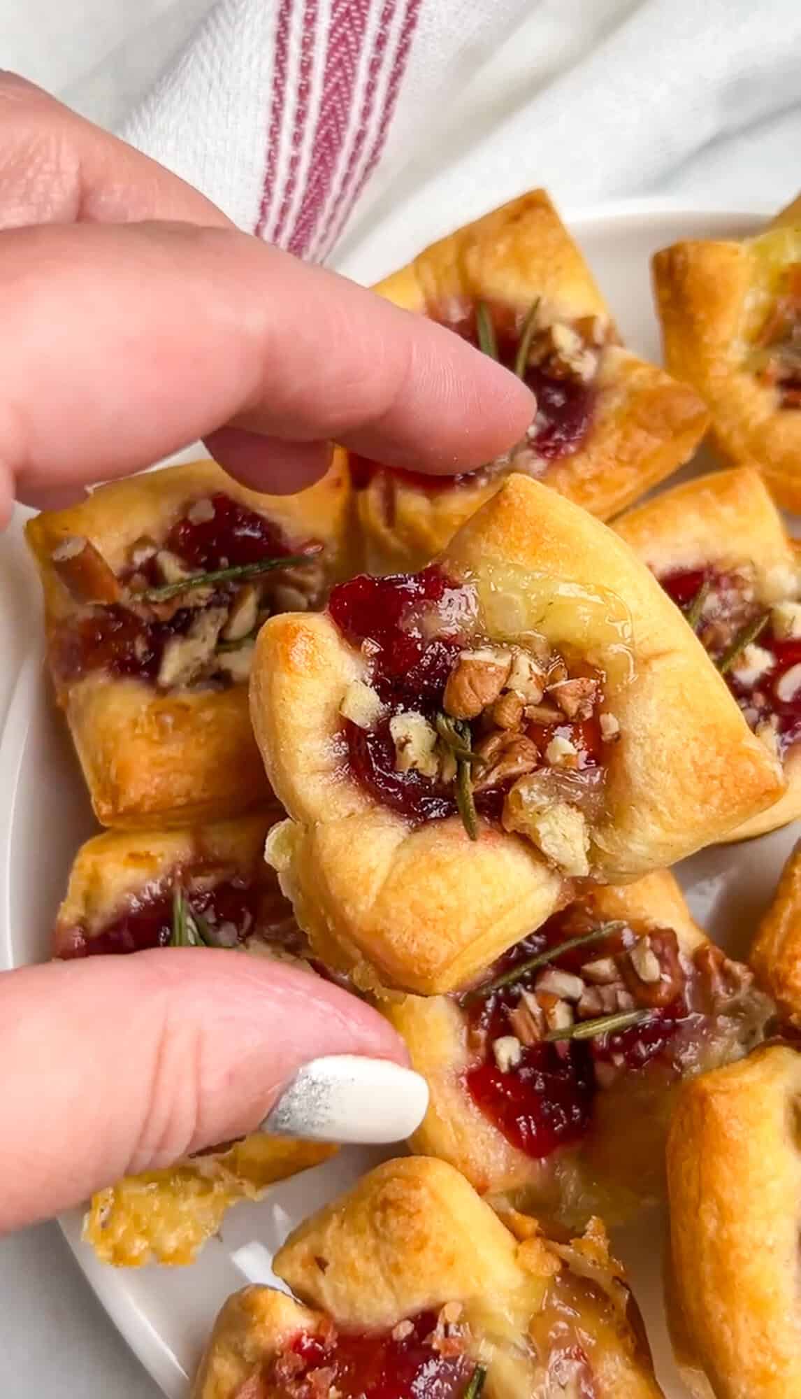 baked brie cranberry bites baked in puff pastry, being held in a hand