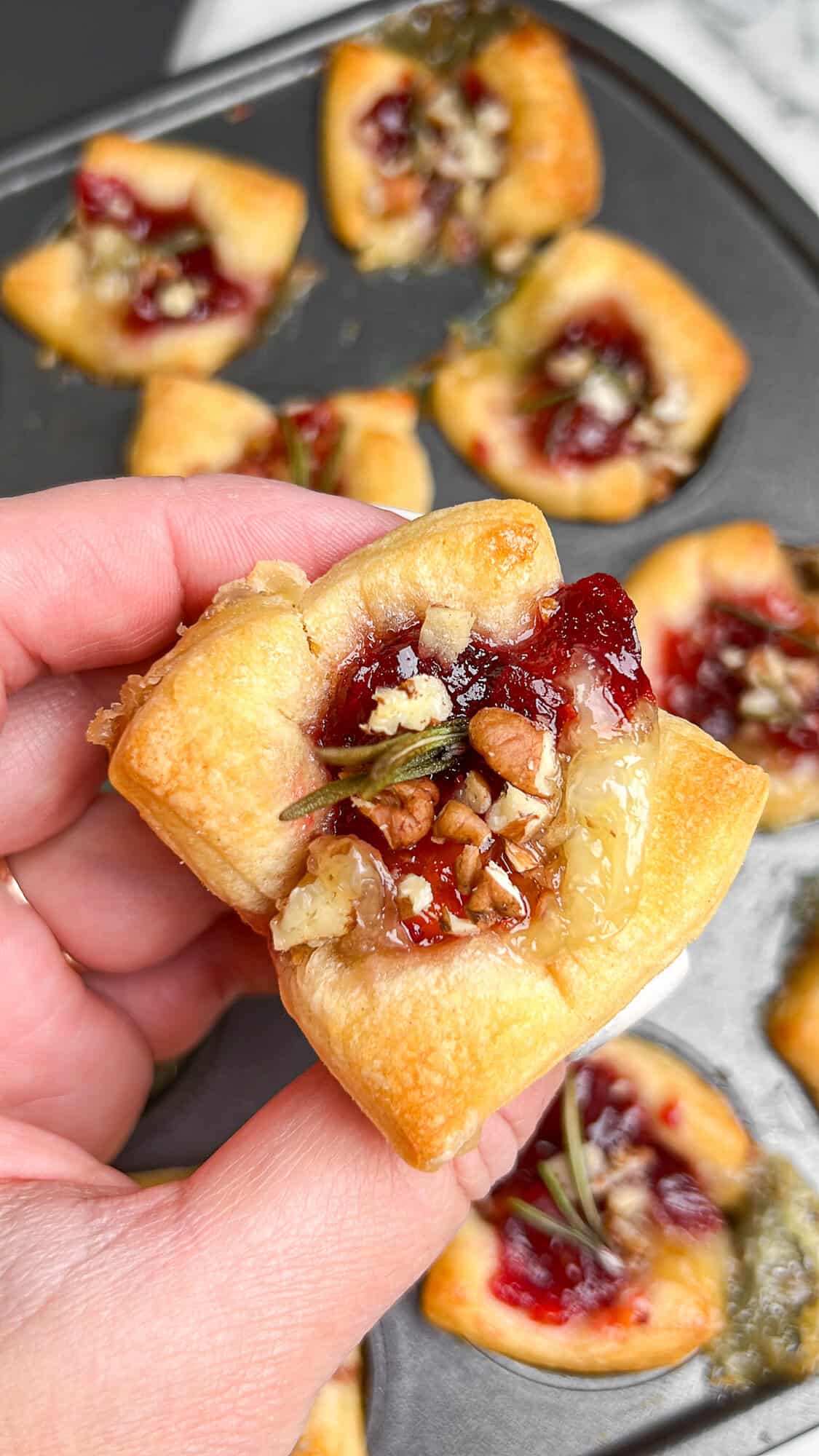 baked brie cranberry bites baked in puff pastry, being held in a hand