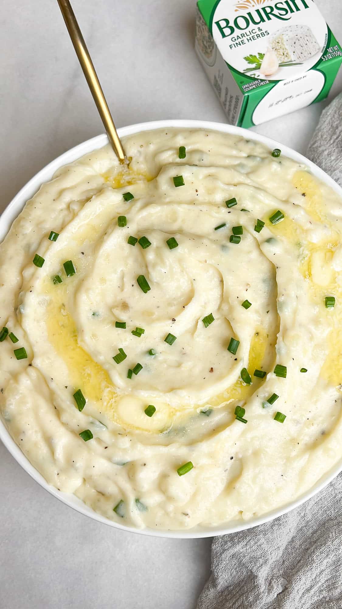 bowl of mashed potatoes with a gold spoon sitting beside a box of boursin cheese