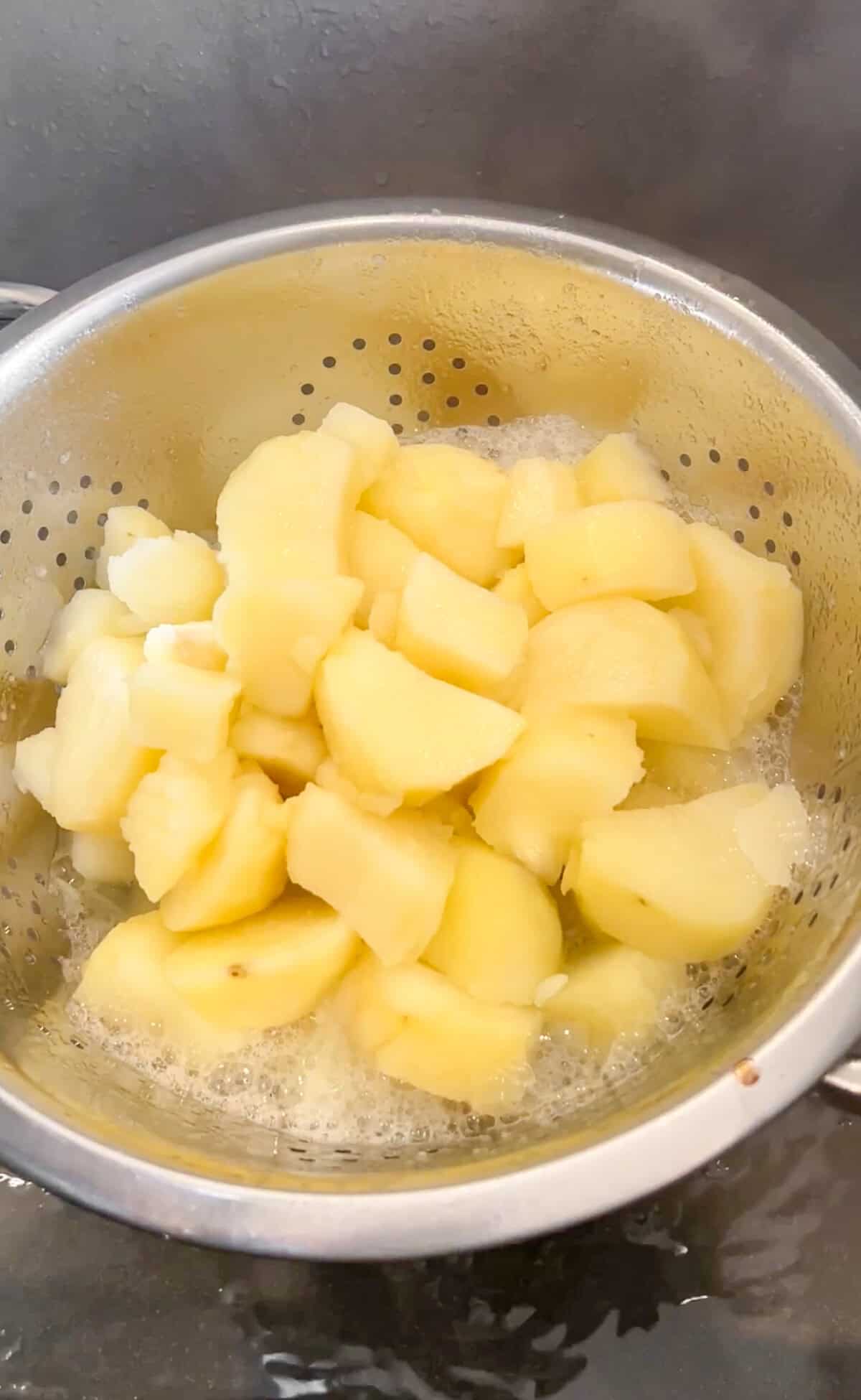 draining hot potato chunks in a strainer in the sink