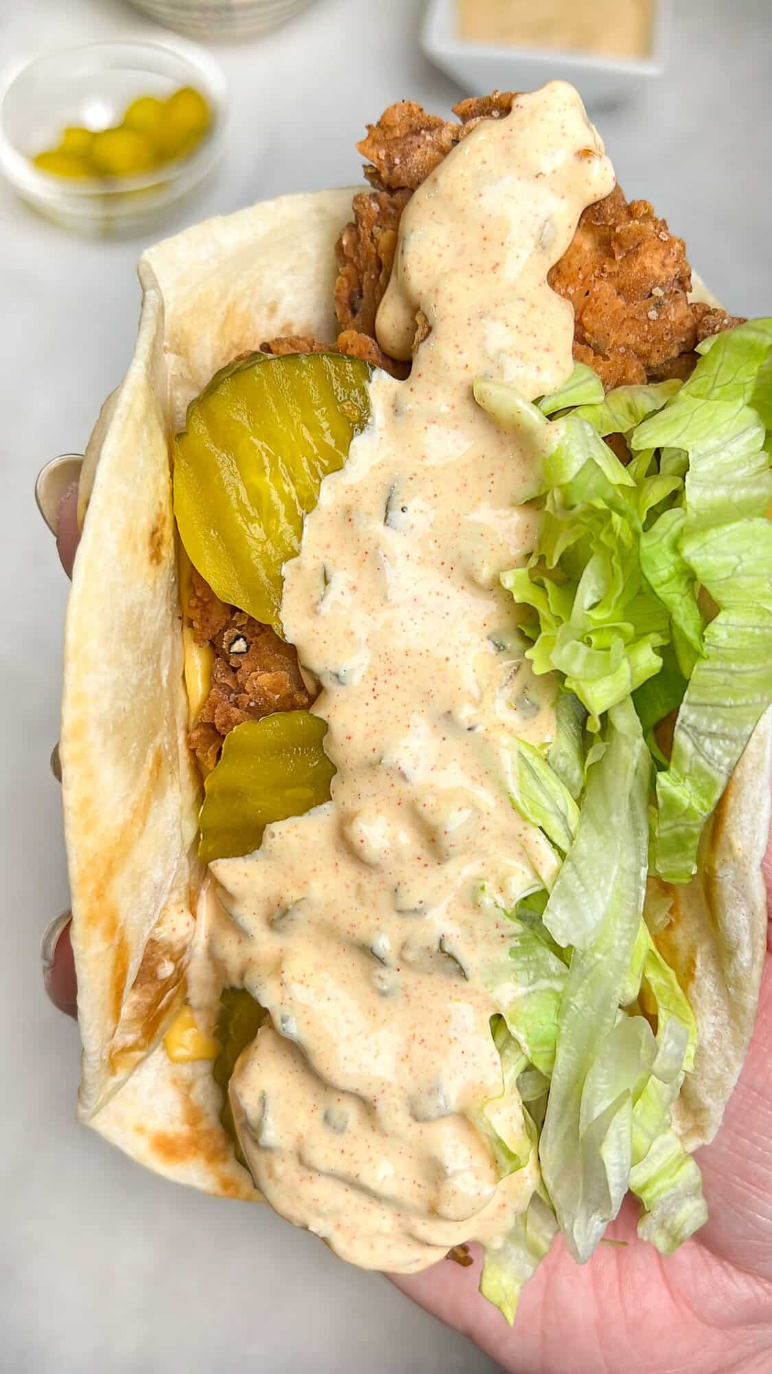 fried chicken taco with pickles and lettuce being held by hand