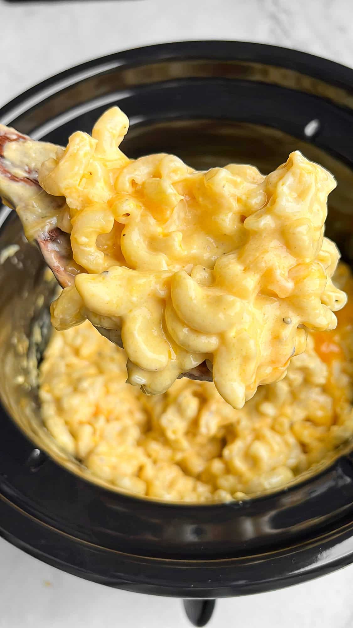 creamy cheese mac and cheese in a slow cooker with a serving spoon