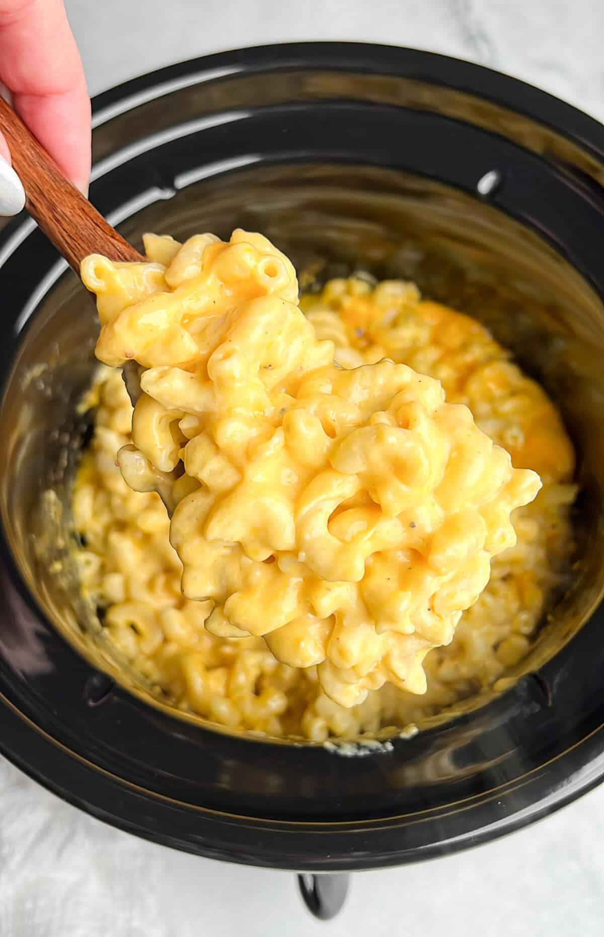 creamy cheese mac and cheese in a slow cooker with a serving spoon