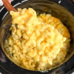 A serving spoon scooping creamy mac and cheese out of a slow cooker.