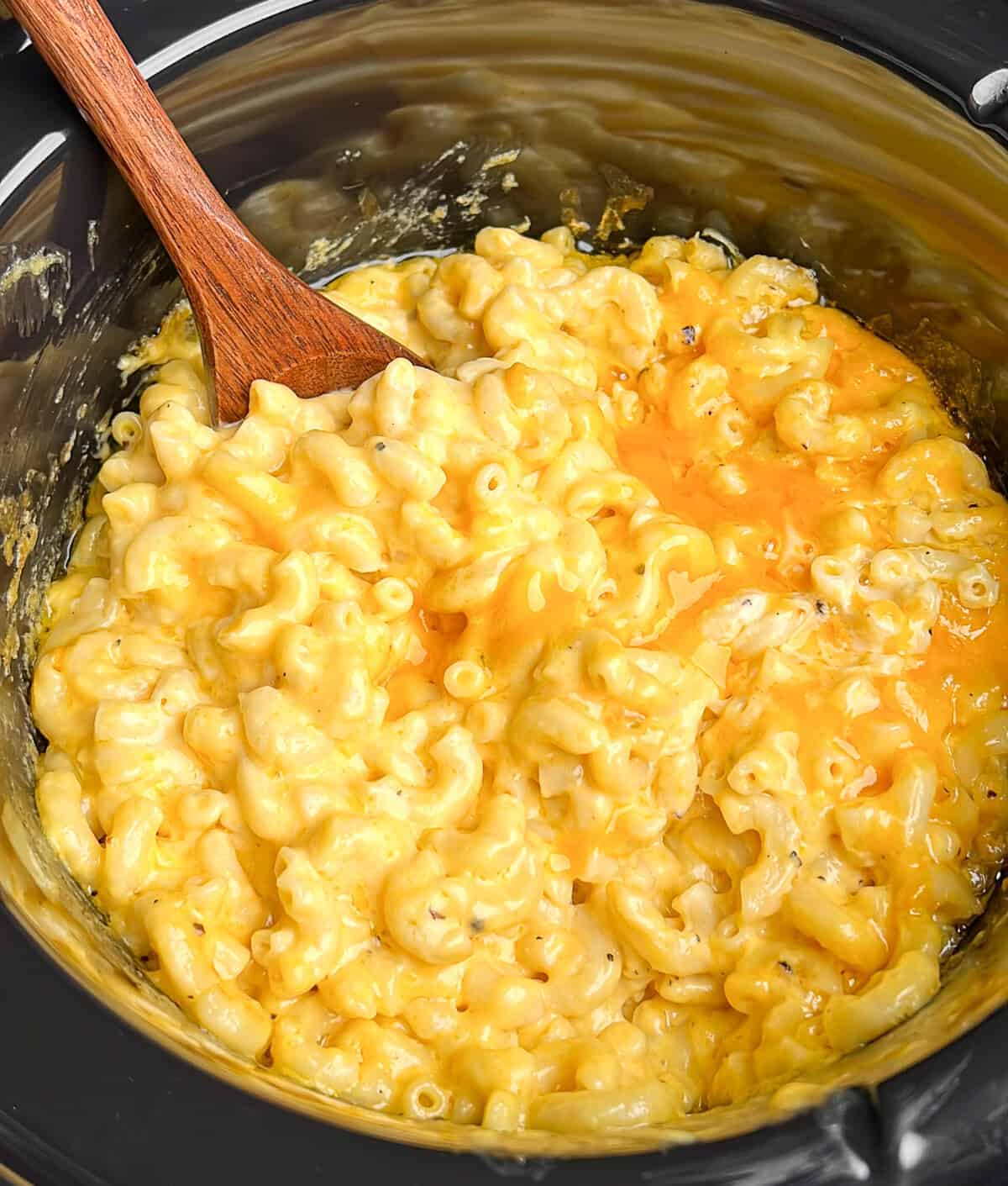 creamy cheese mac and cheese in a slow cooker with a serving spoon