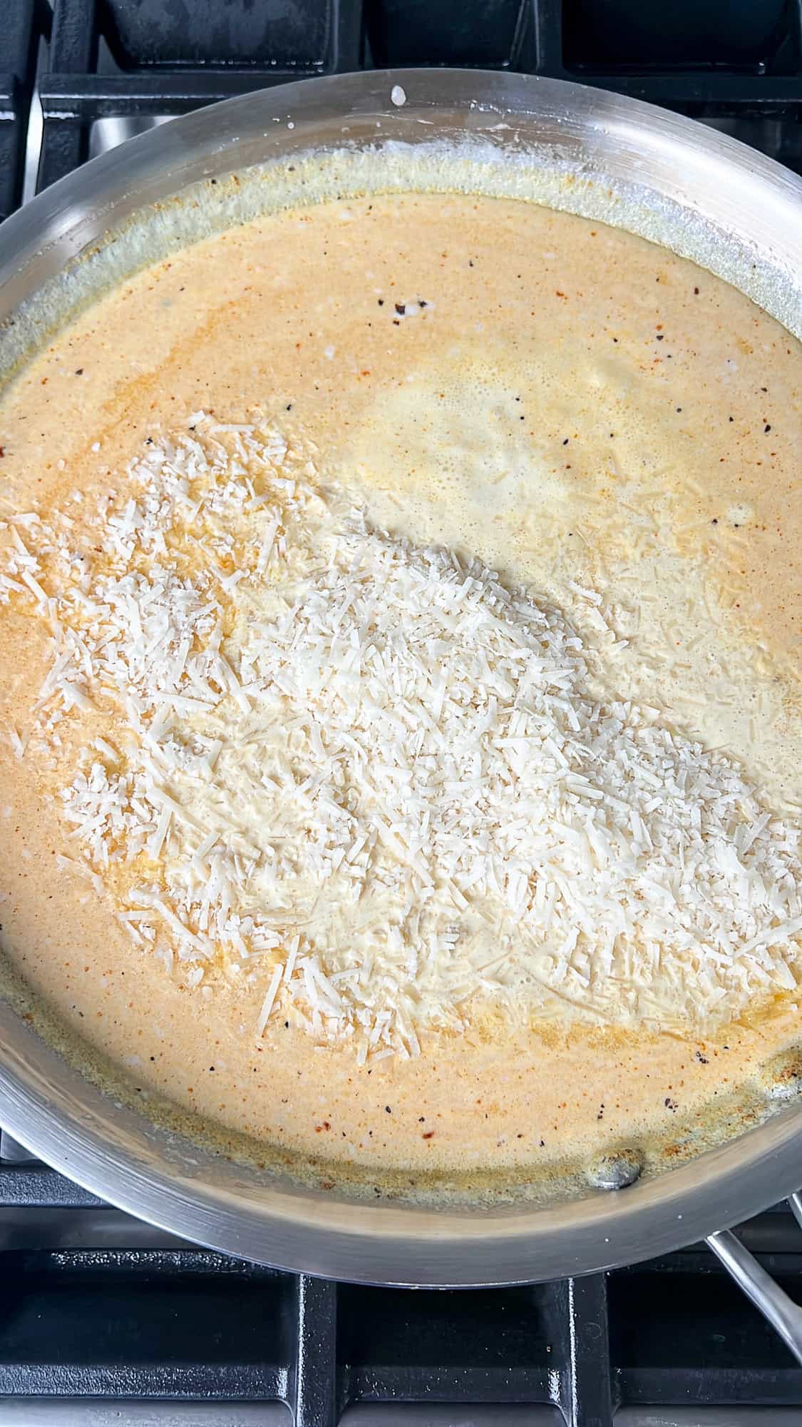 adding parmesan to the alfredo sauce in a pan