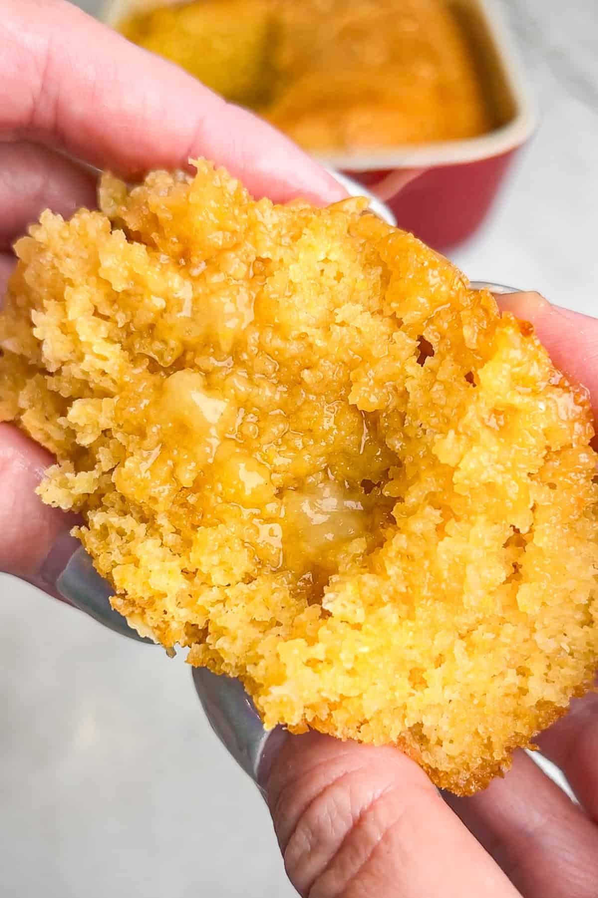 This moist, tender honey butter cornbread is full of real corn flavor and doused in a buttery, sticky glaze. It's ready for the holidays. Hands holding a big slice of honey butter cornbread up to the camera to show the moist interior.