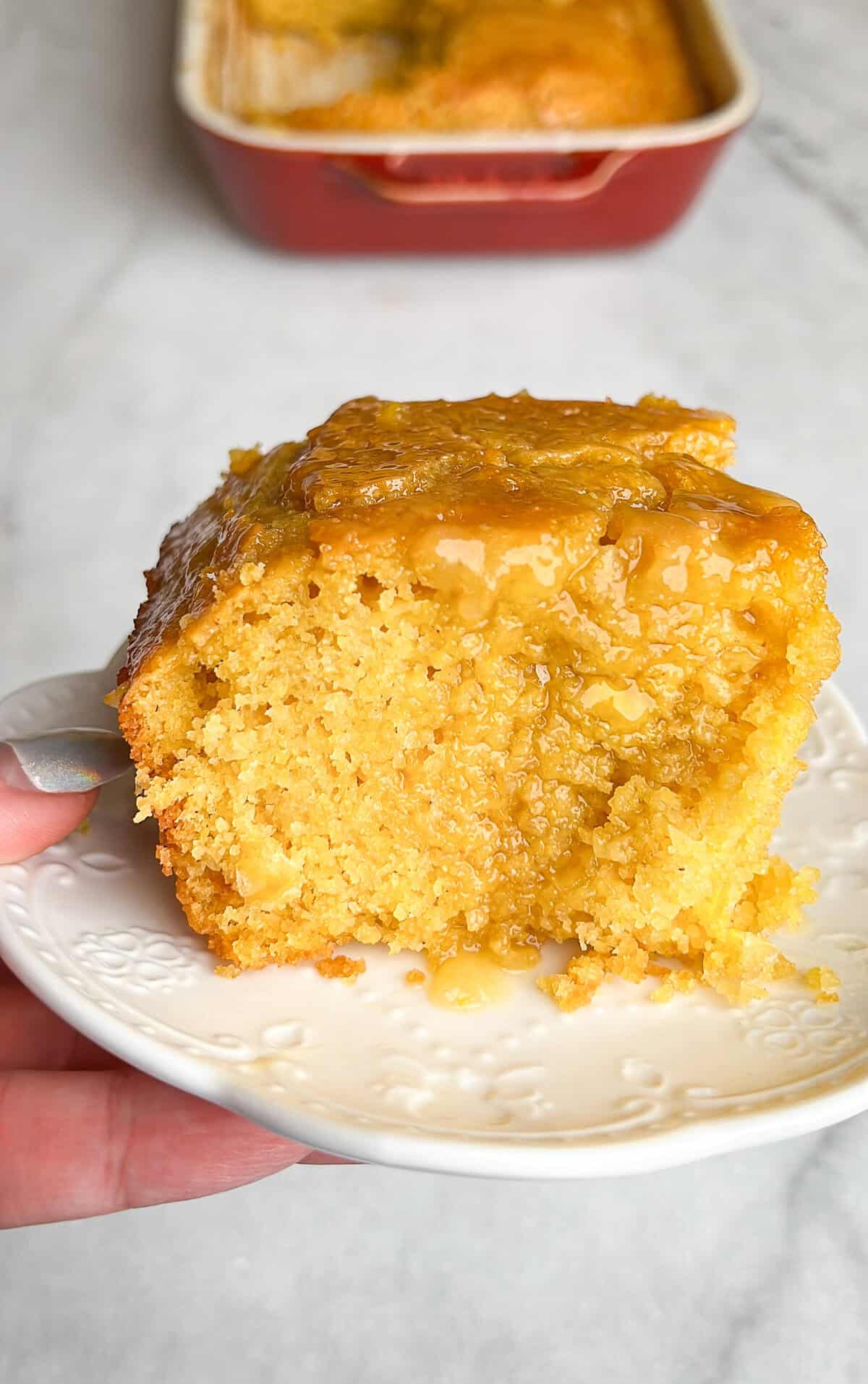 This moist, tender honey butter cornbread is full of real corn flavor and doused in a buttery, sticky glaze. It's ready for the holidays. A big hunk of honey butter cornbread on a plate.