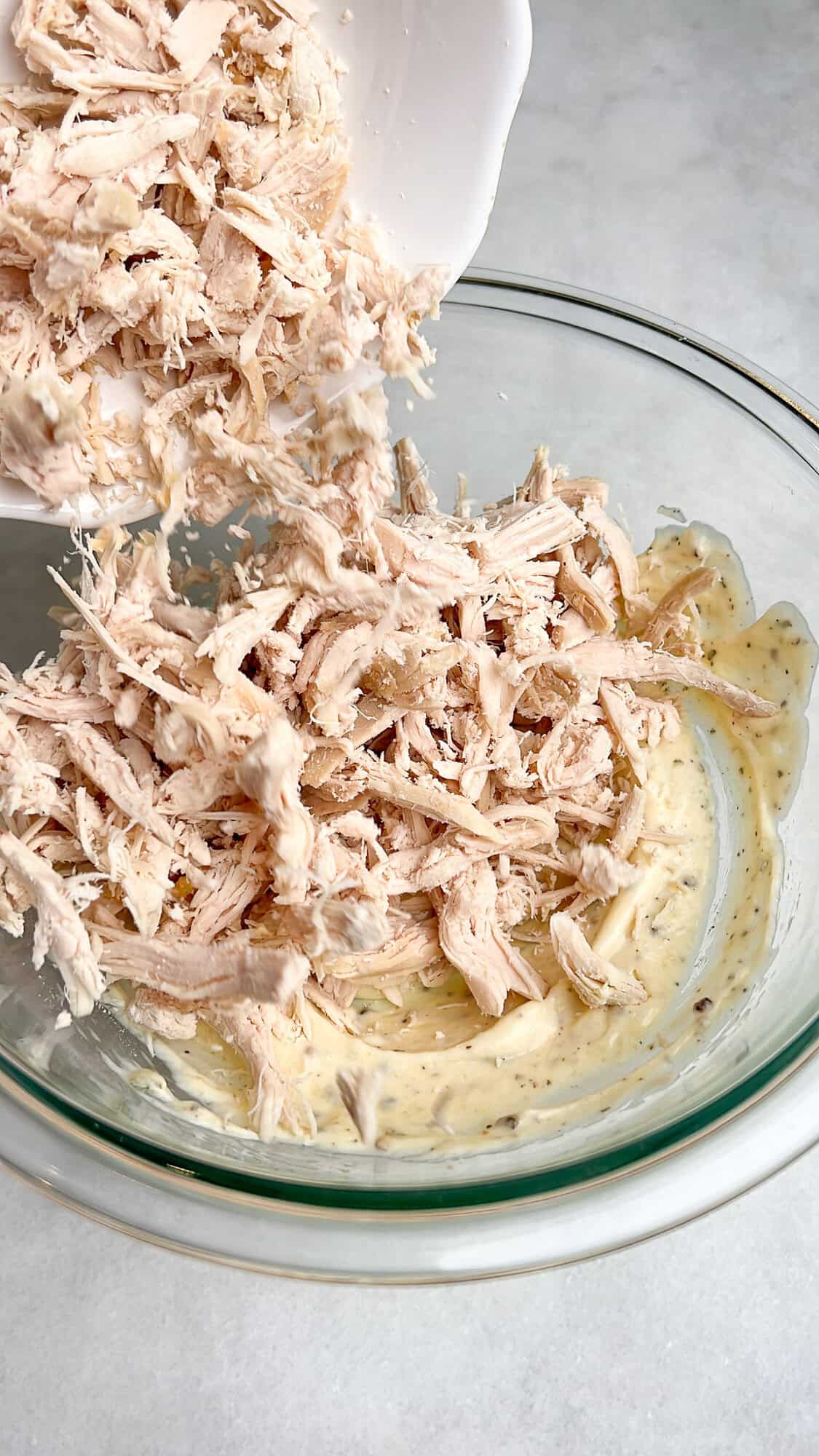 pouring in the shredded chicken into the dressing