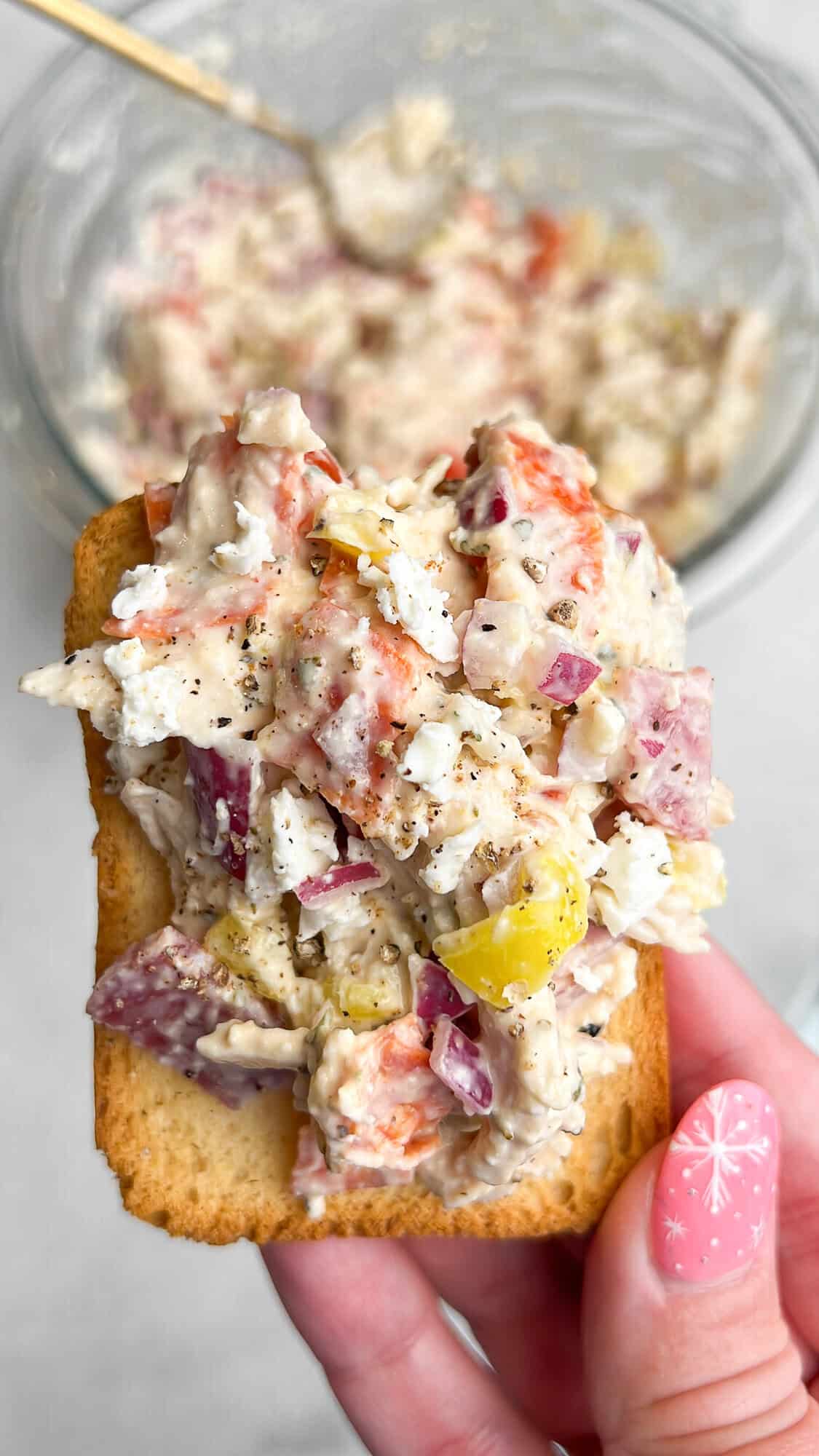 chicken salad piled on a cracker being held by hand.